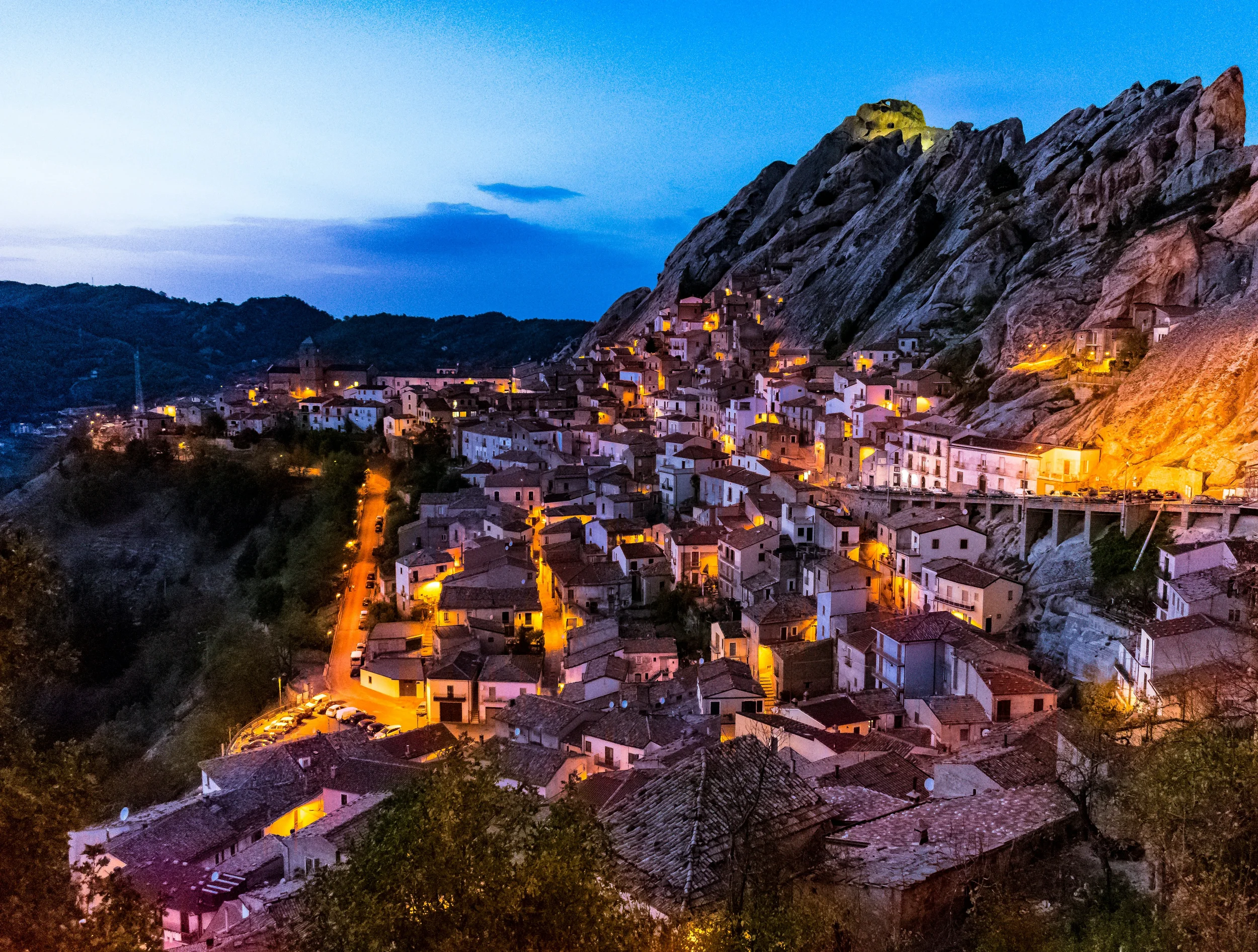 Pietrapertosa at dusk, with illuminated houses beneath a steep rocky ridge in Basilicata.