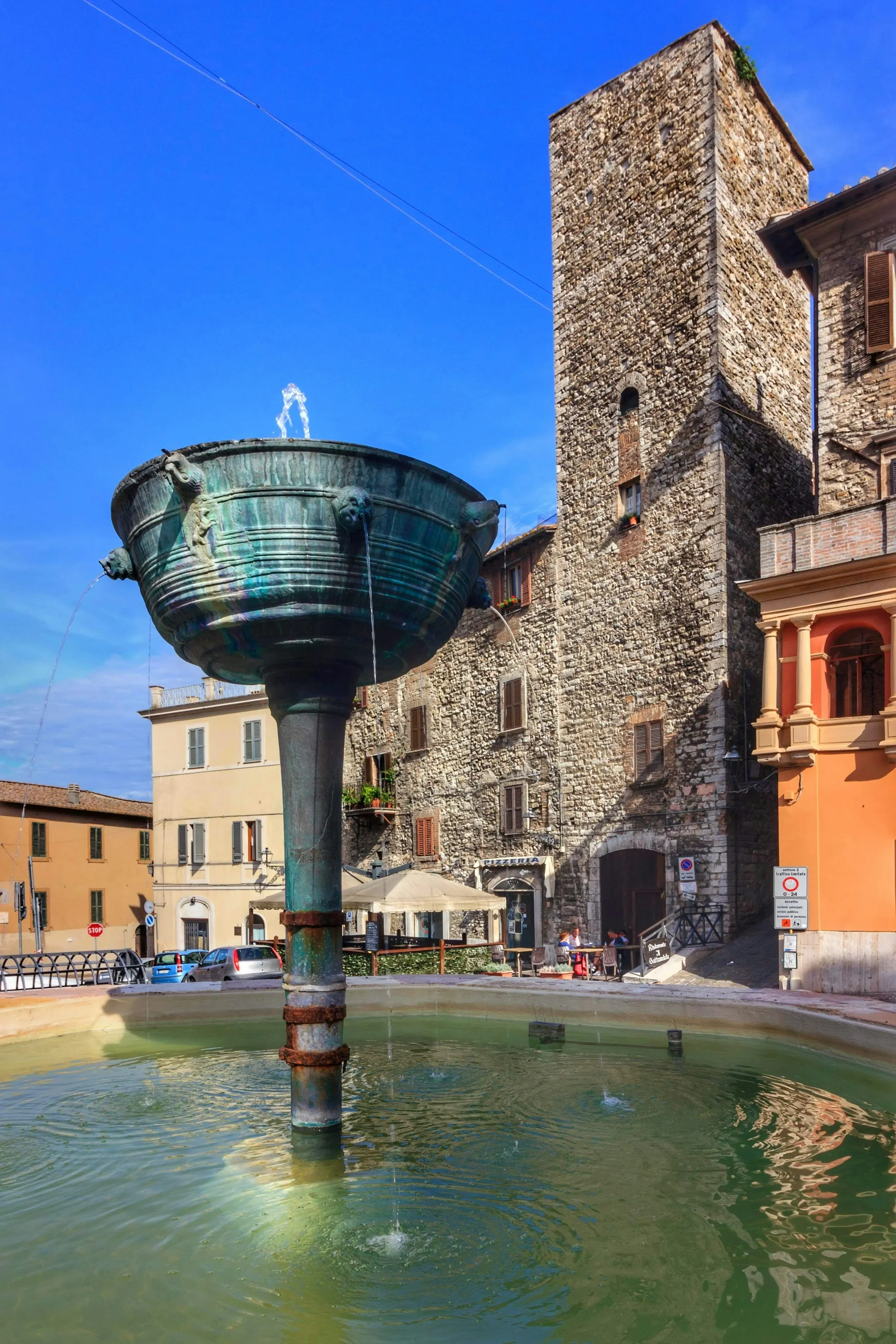 Historic fountain and stone tower on a sunlit square in Narni