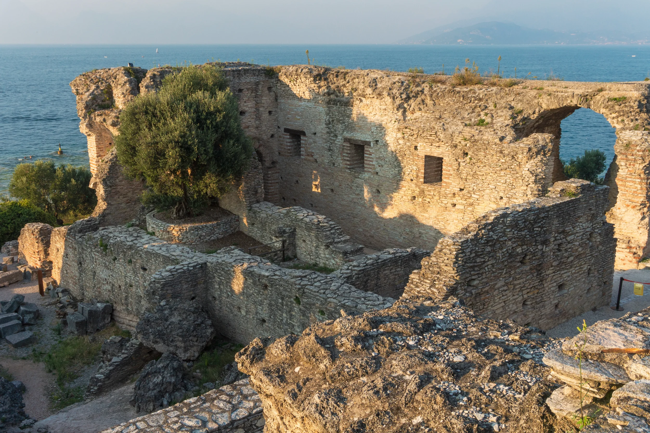 Sunlit stone walls and an arch at the Grotte di Catullo Roman villa, with Lake Garda beyond.