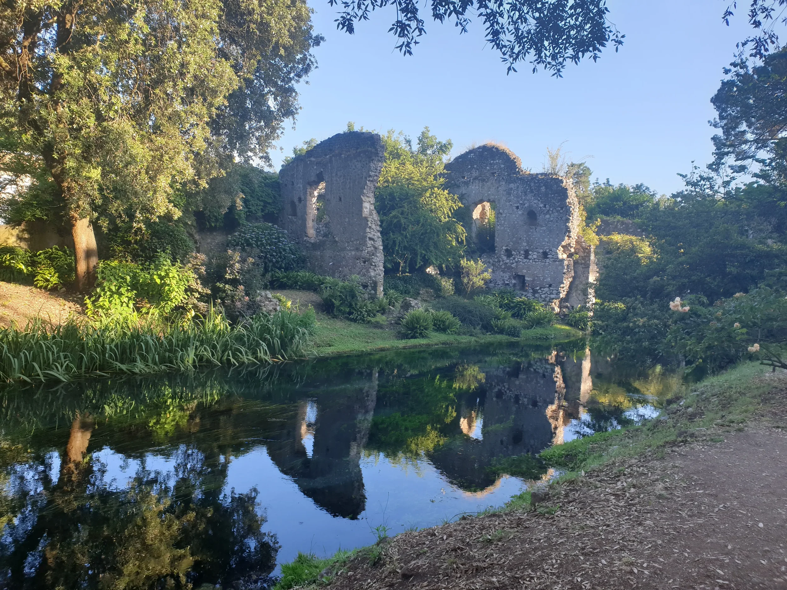 Medieval stone walls and arched windows mirrored in the still water at Giardino di Ninfa.