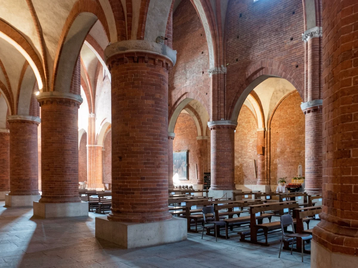 Brick columns and vaulted arches inside Morimondo Abbey, with rows of wooden chairs.