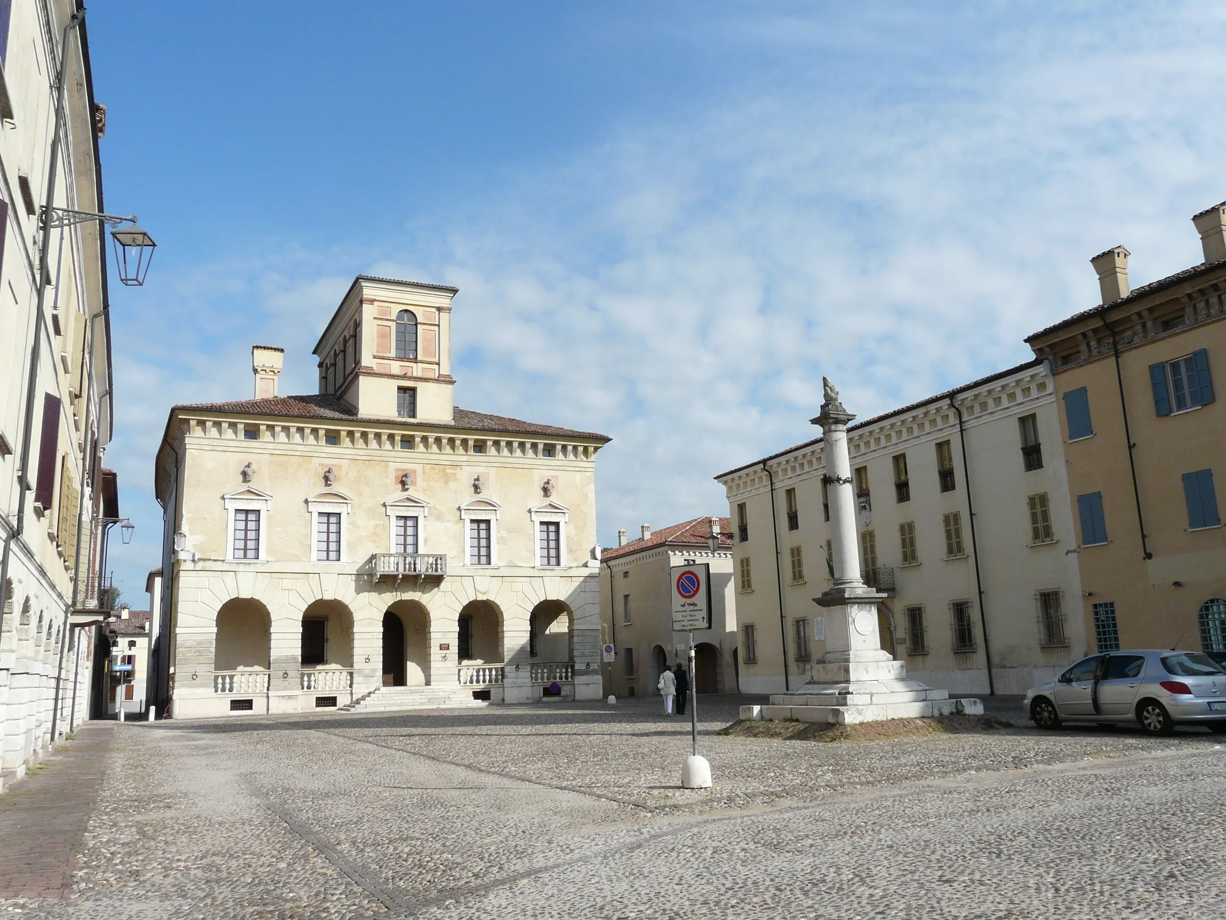 Piazza Ducale in Sabbioneta, with the arcaded town hall and a stone column beneath a blue sky.
