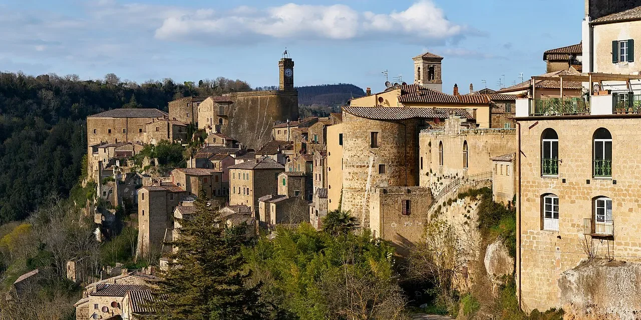 Sorano’s stone houses and walls above a wooded valley, with the clock tower of Masso Leopoldino on the skyline.