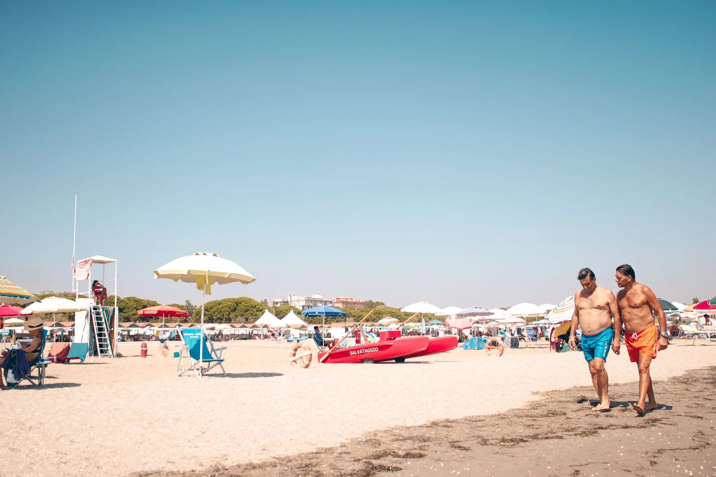 Sandy beach in Sicily with colourful umbrellas, beachgoers and turquoise Mediterranean water under a clear blue sky