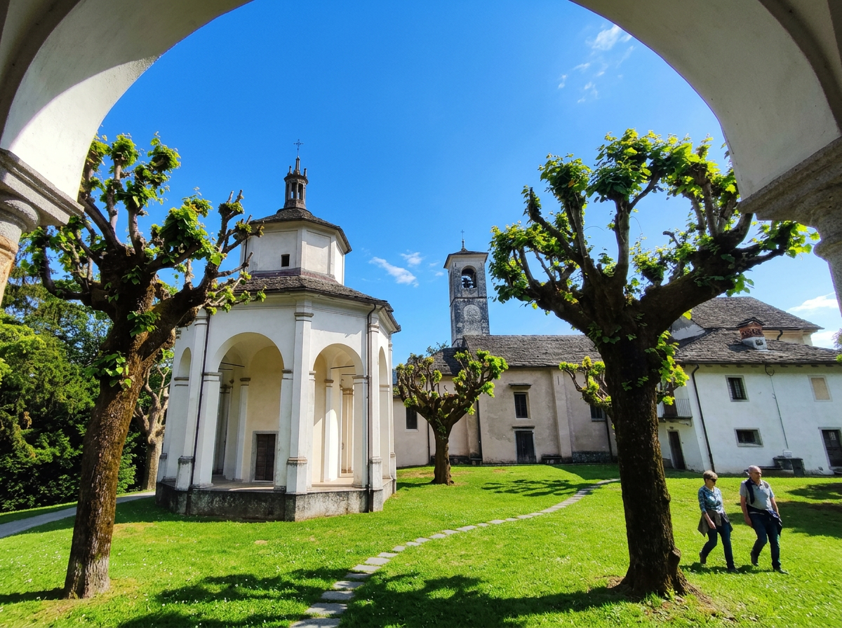 White chapel and bell tower at Sacro Monte di Ghiffa, framed by trees and an archway