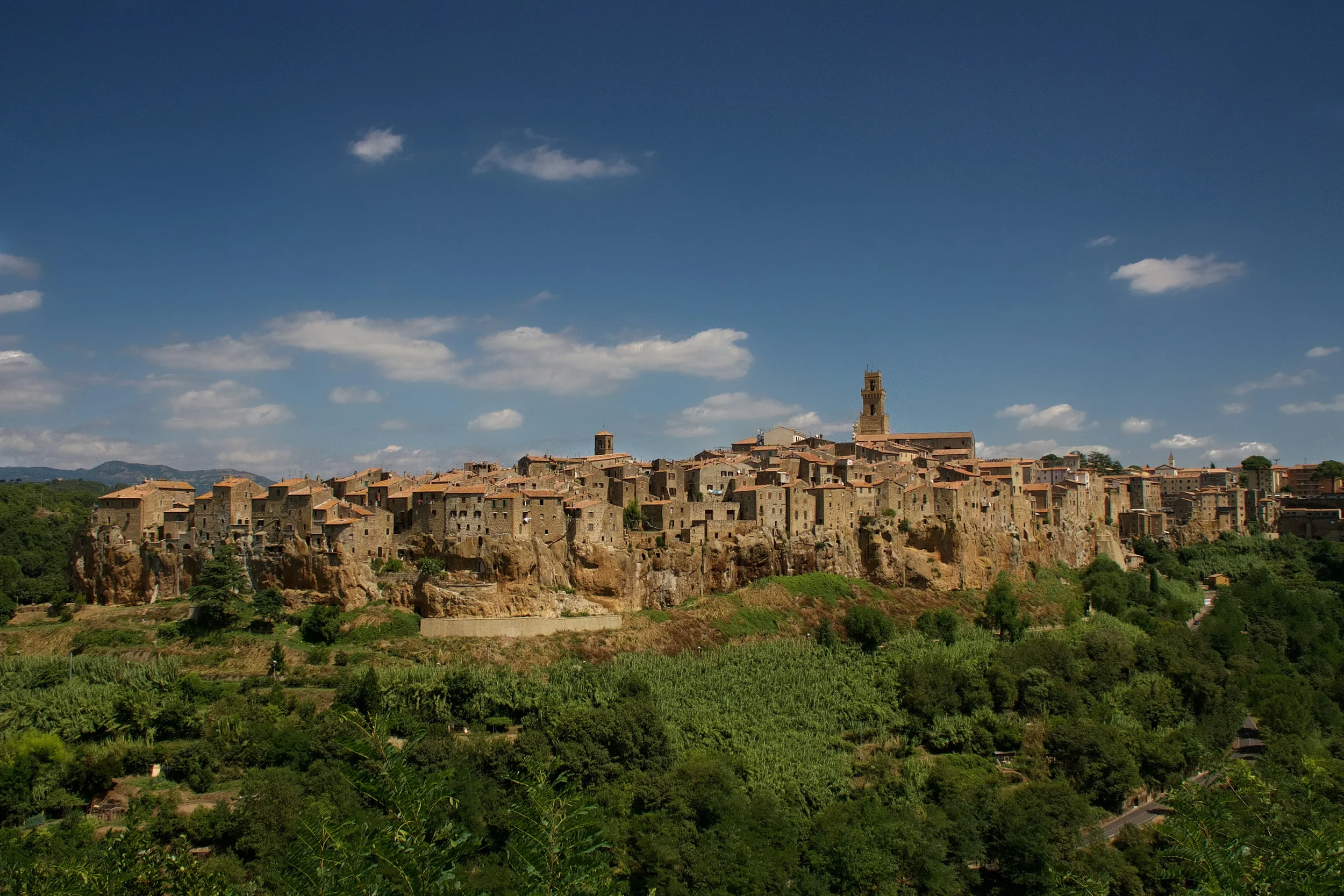 Pitigliano’s stone houses and cathedral tower rising above a tuff cliff and wooded valley in Tuscany.