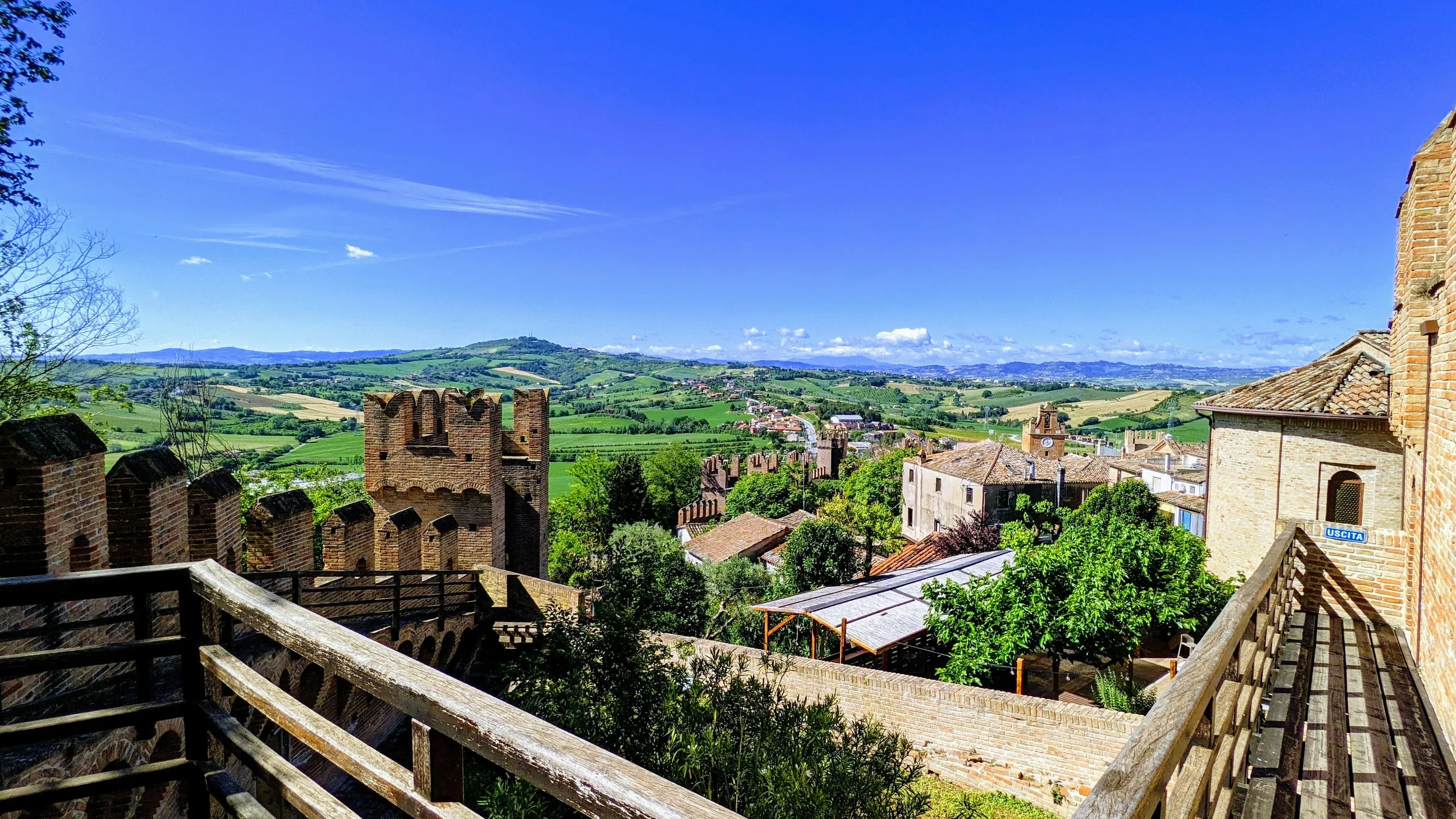 View from Gradara castle across brick battlements, village rooftops and the green hills of Le Marche