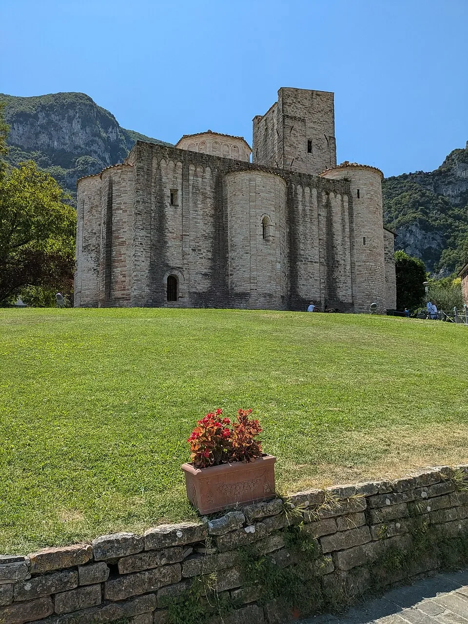 The rounded stone apses and square tower of San Vittore alle Chiuse above a green lawn