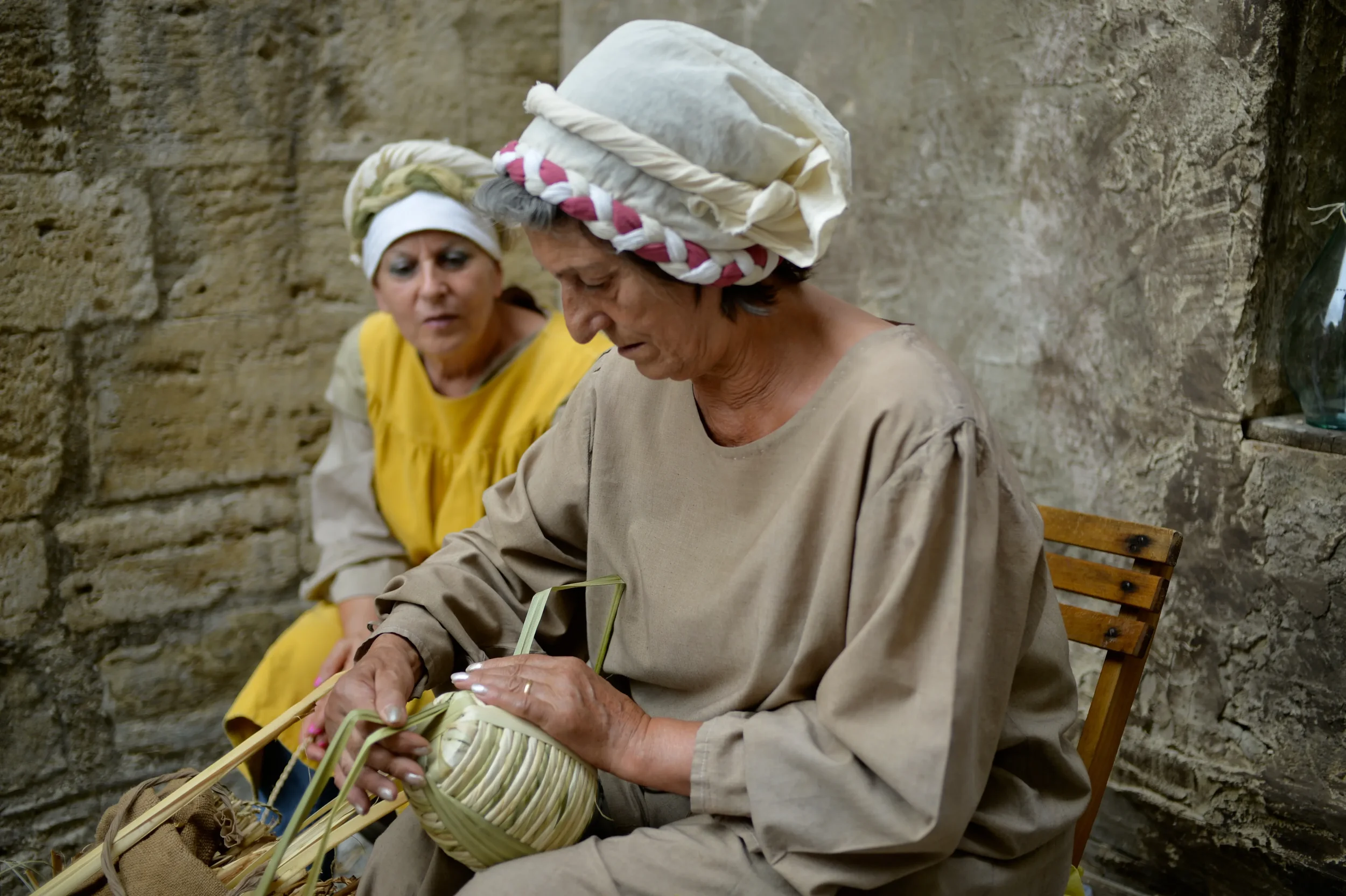 Two women in medieval dress demonstrating basket weaving during a historical festival in Bevagna