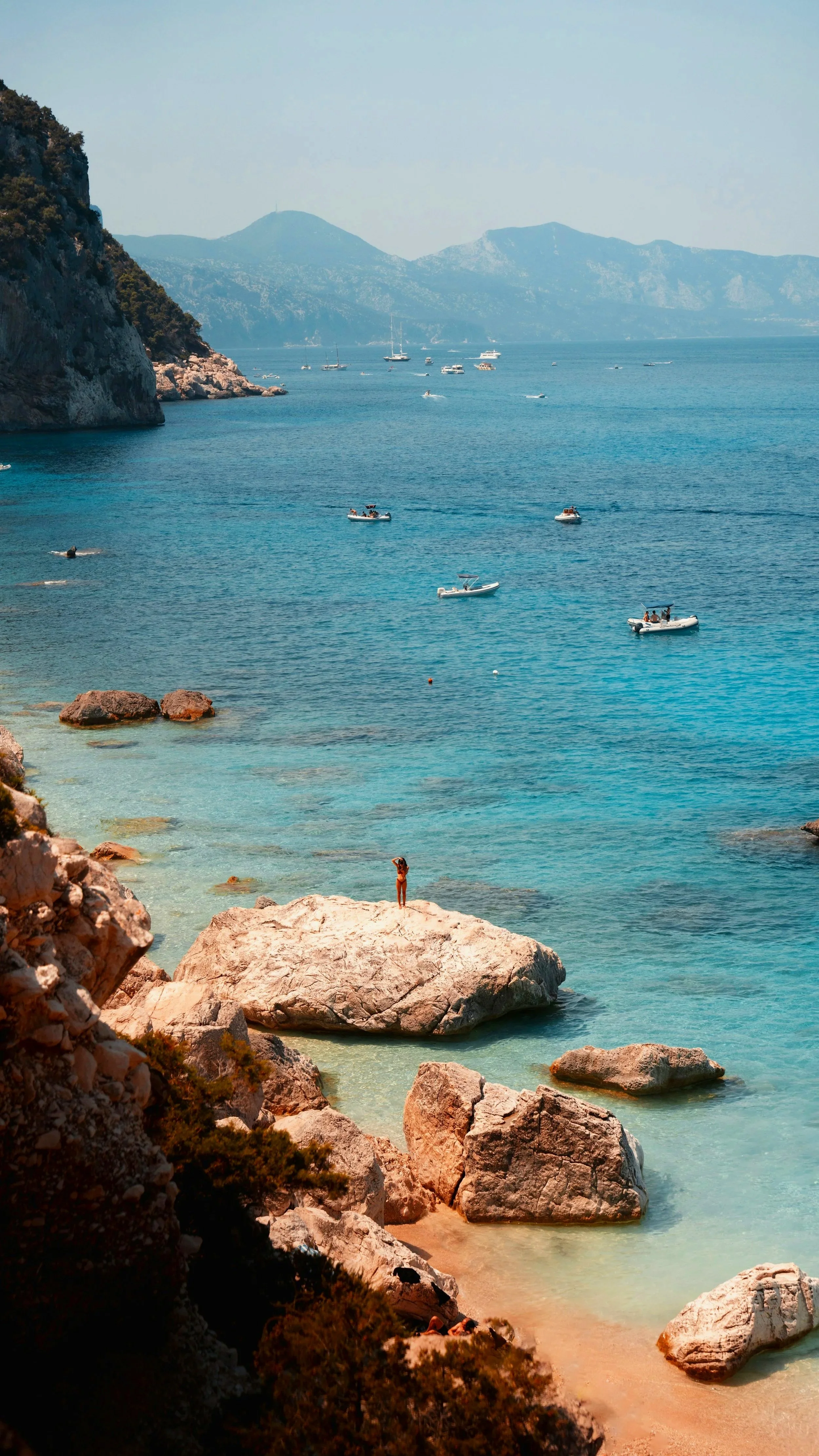Cala Mariolu in Sardinia with turquoise water, anchored boats and large white limestone rocks along the rugged coastline