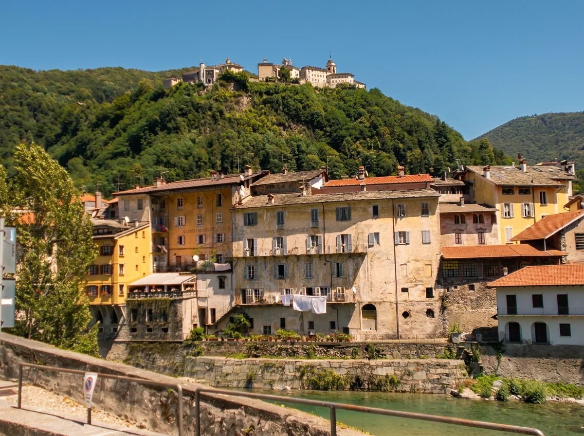 Historic riverside houses in Varallo beneath the wooded hill of the Sacro Monte.