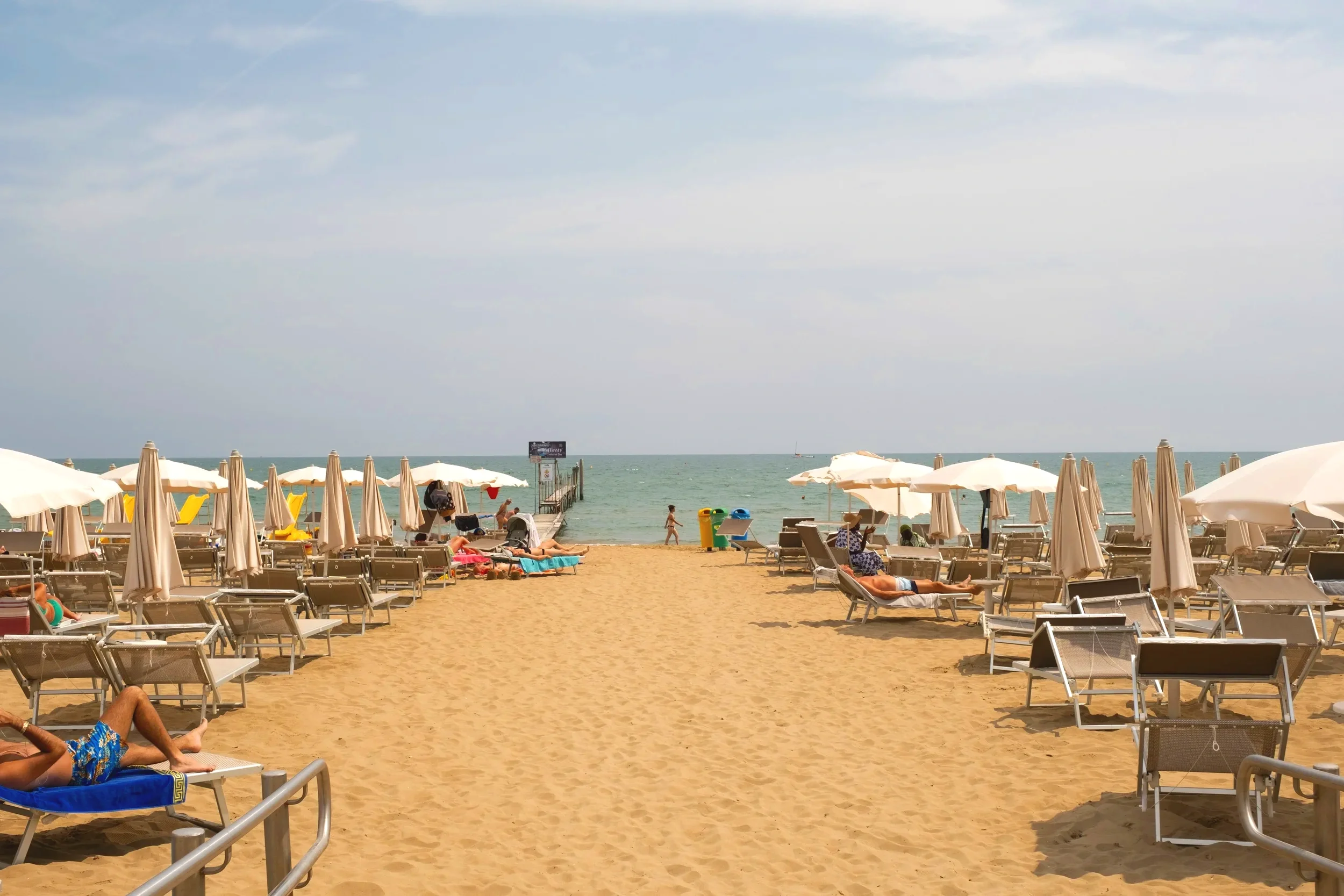 Sandy beach in Tuscany with rows of sun loungers and umbrellas overlooking the calm Tyrrhenian Sea.