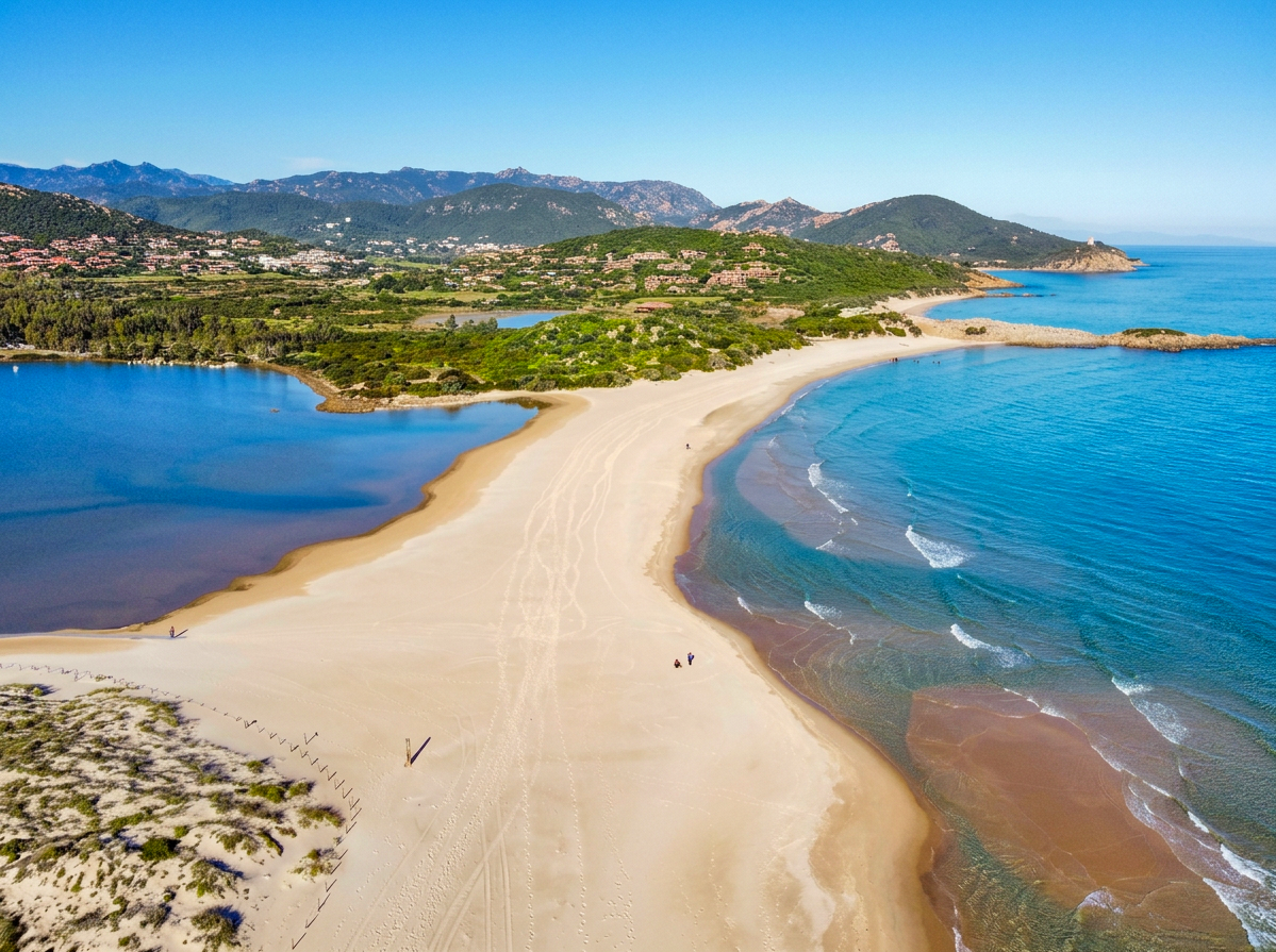 Aerial view of Spiaggia di Su Giudeu in Sardinia, with golden sand, blue water, coastal dunes and a lagoon surrounded by green hills