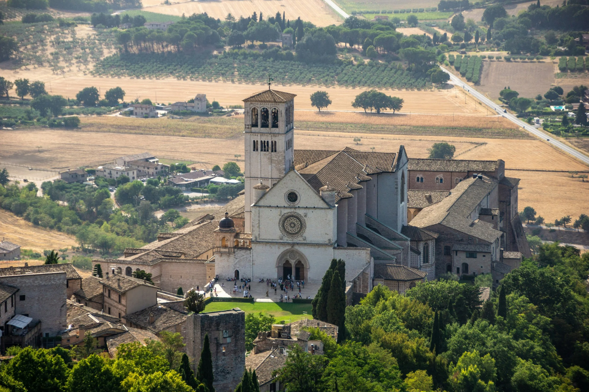 Basilica of Saint Francis in Assisi, with its bell tower and rose window overlooking the golden fields of Umbria.