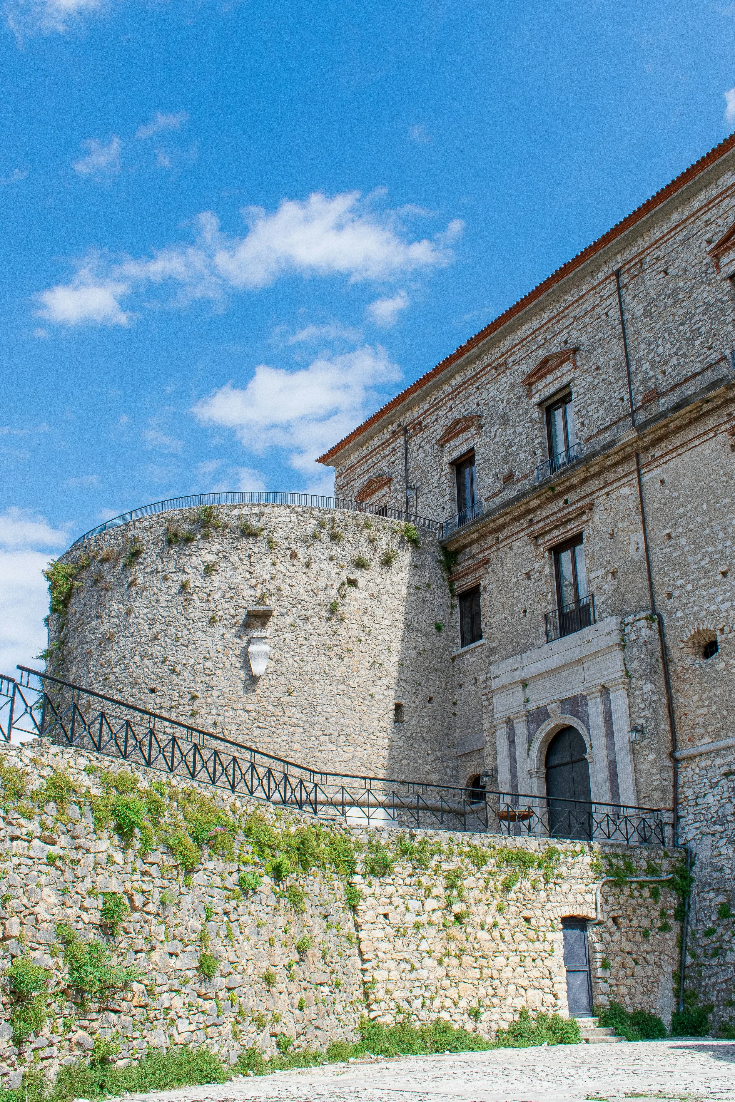 Round stone tower and arched entrance of Teggiano’s castle, beside a sloping walkway.