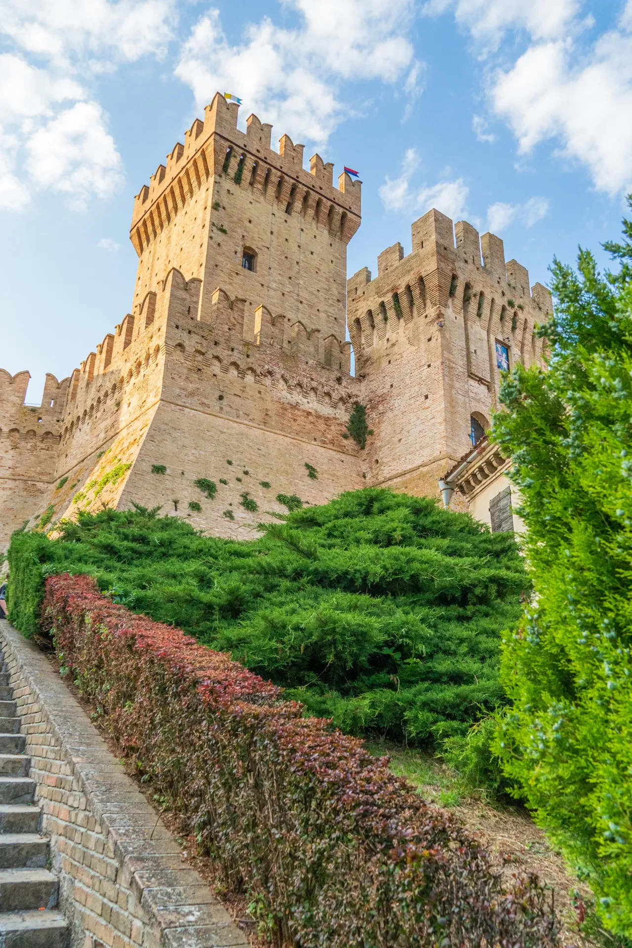Crenellated tower of the Rocca di Offagna rising above planted slopes and a stone stairway