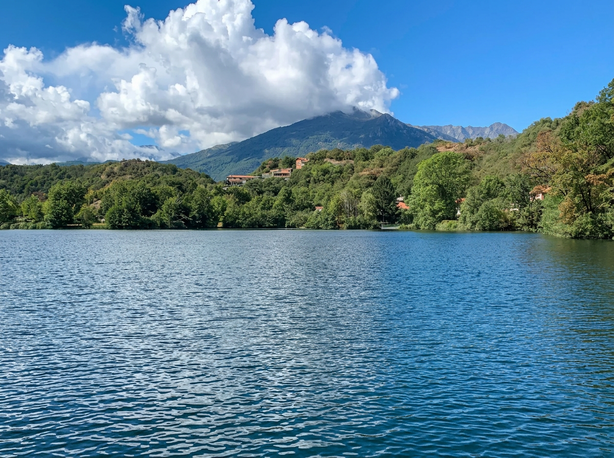 Lago Sirio surrounded by wooded hills, with mountains beneath a cloudy sky near Ivrea, Piemonte, Italy.