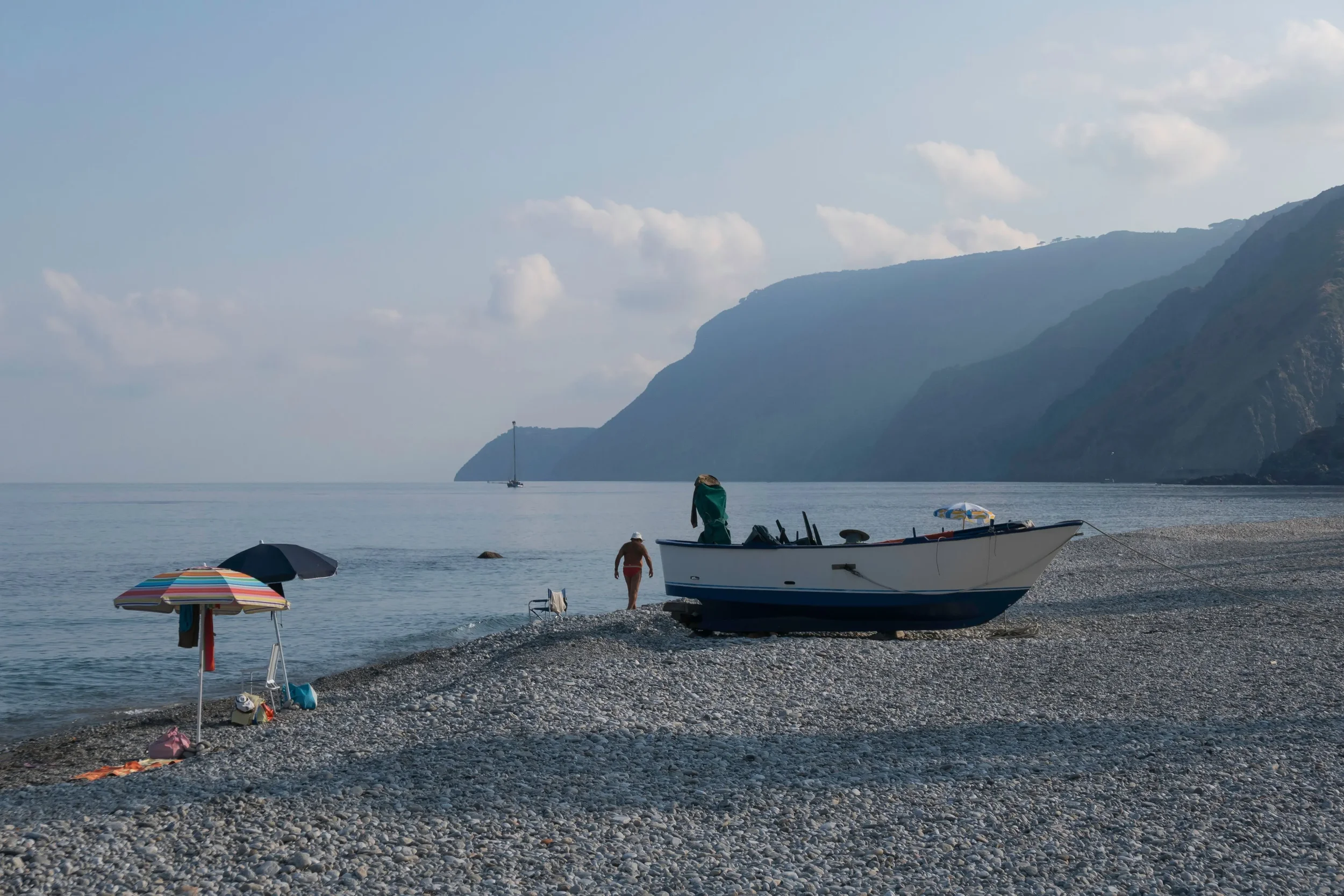 Pebble beach with a fishing boat, colourful parasols and dramatic mountains along the Calabria coastline in southern Italy.