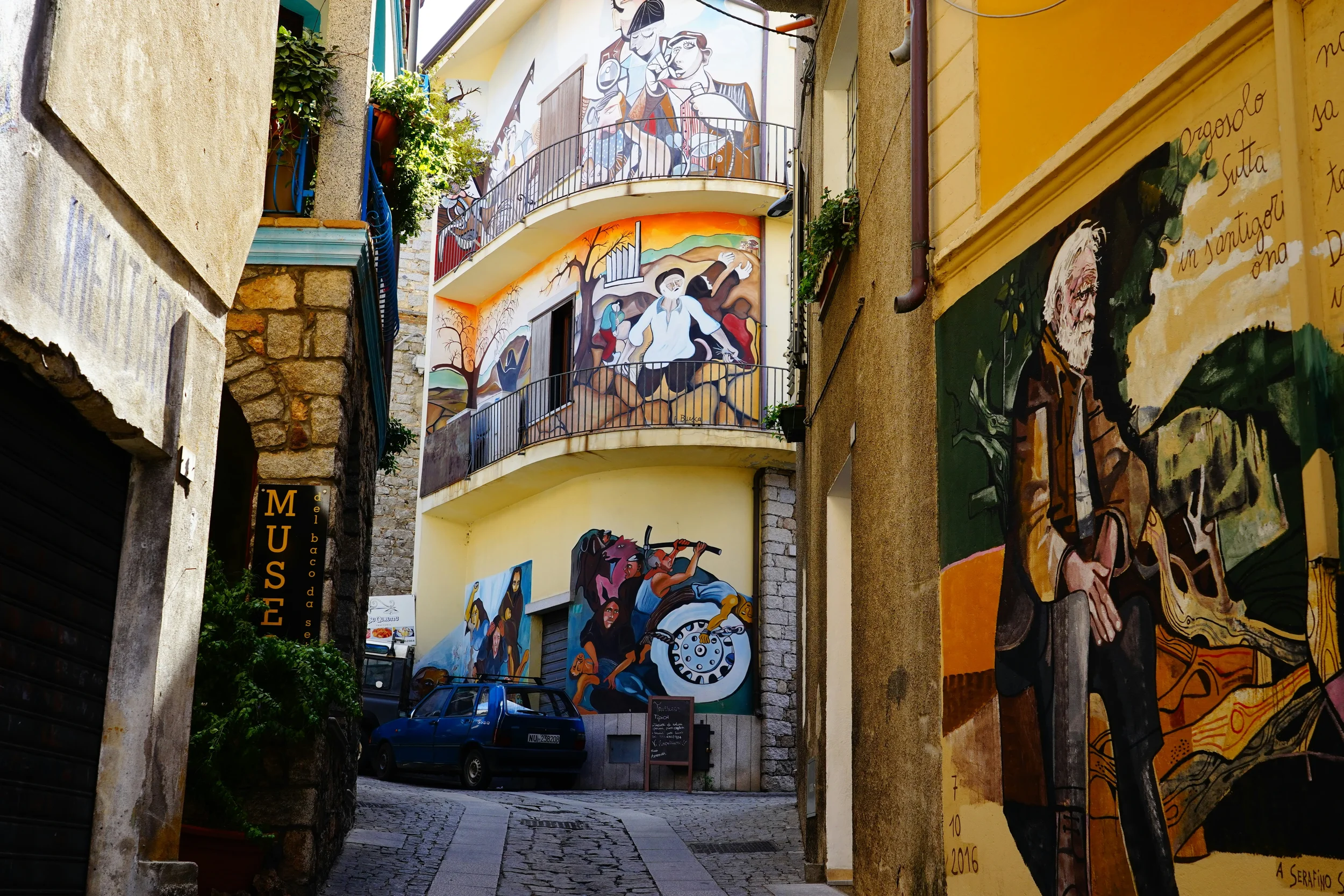 Colourful murals covering buildings along a narrow street in Orgosolo, Sardinia