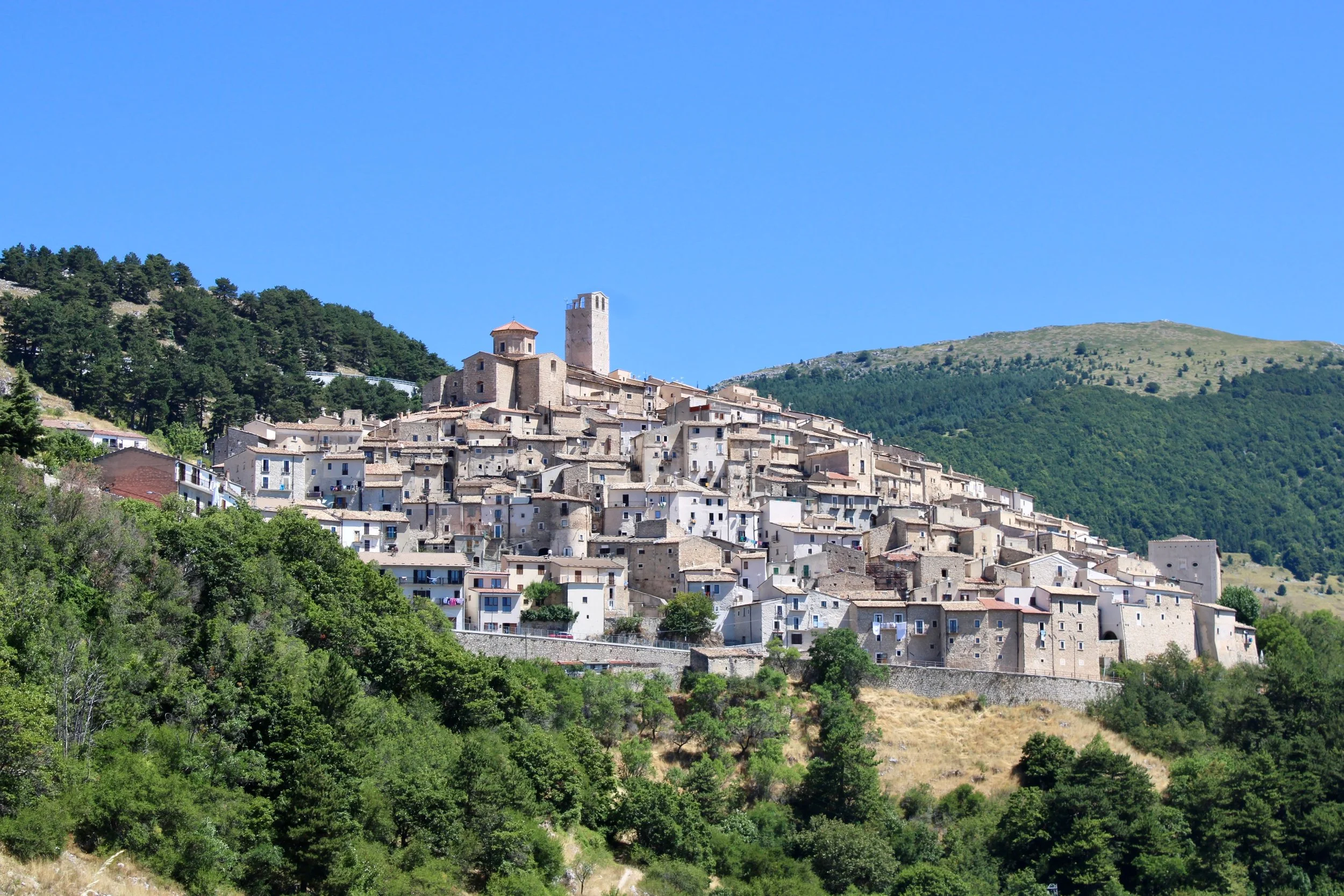 Stone houses and a hilltop church in Castelvecchio Calvisio, surrounded by the mountains of Abruzzo.