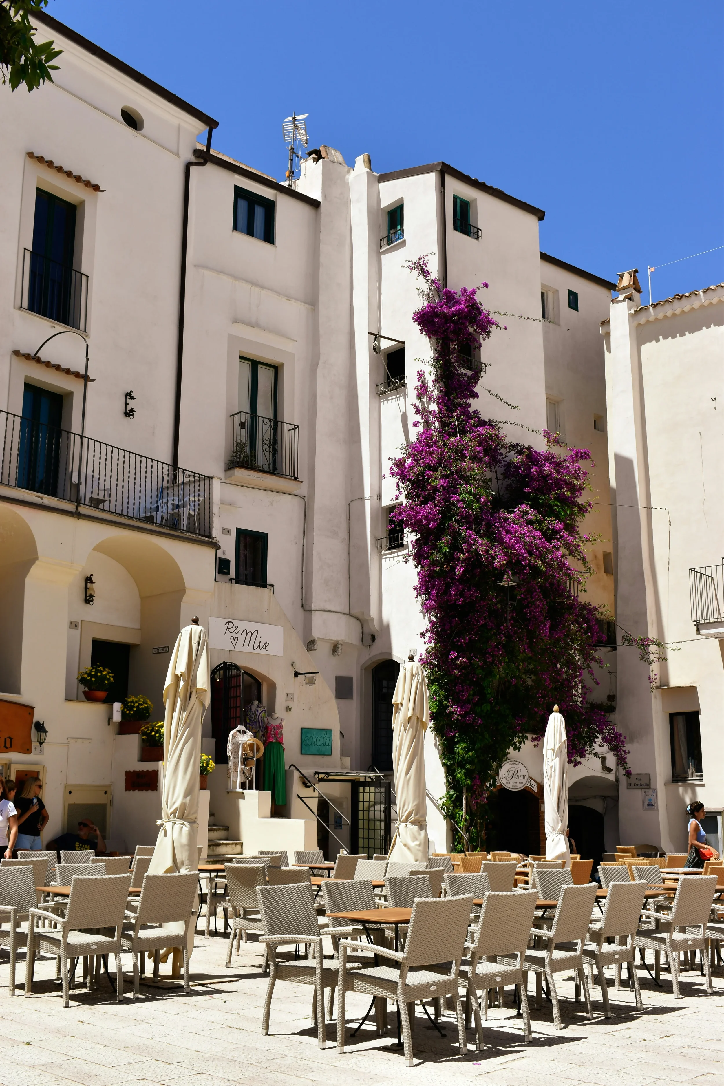 Café tables and chairs beneath white houses and flowering bougainvillea in Sperlonga’s old town.