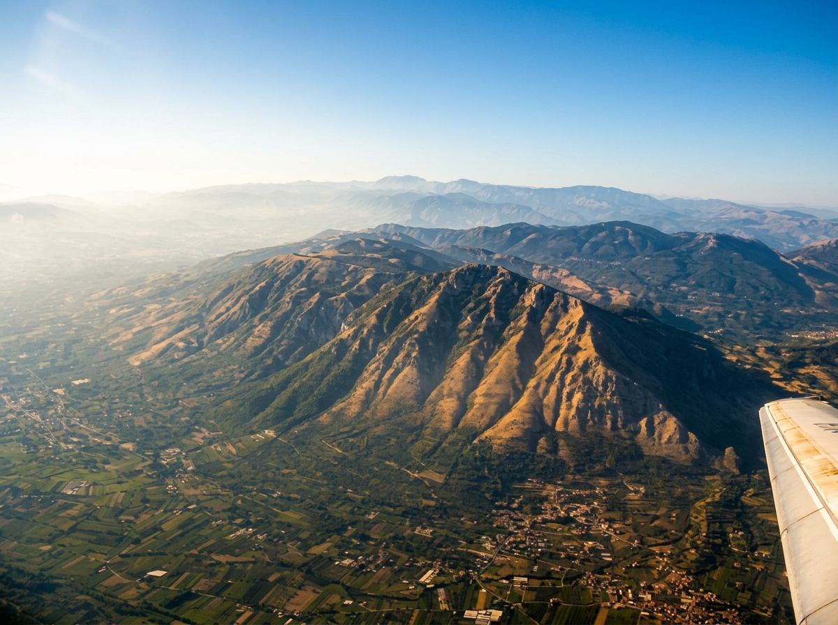 Aerial view of rugged mountain ridges, farmland and villages beneath a clear blue sky.