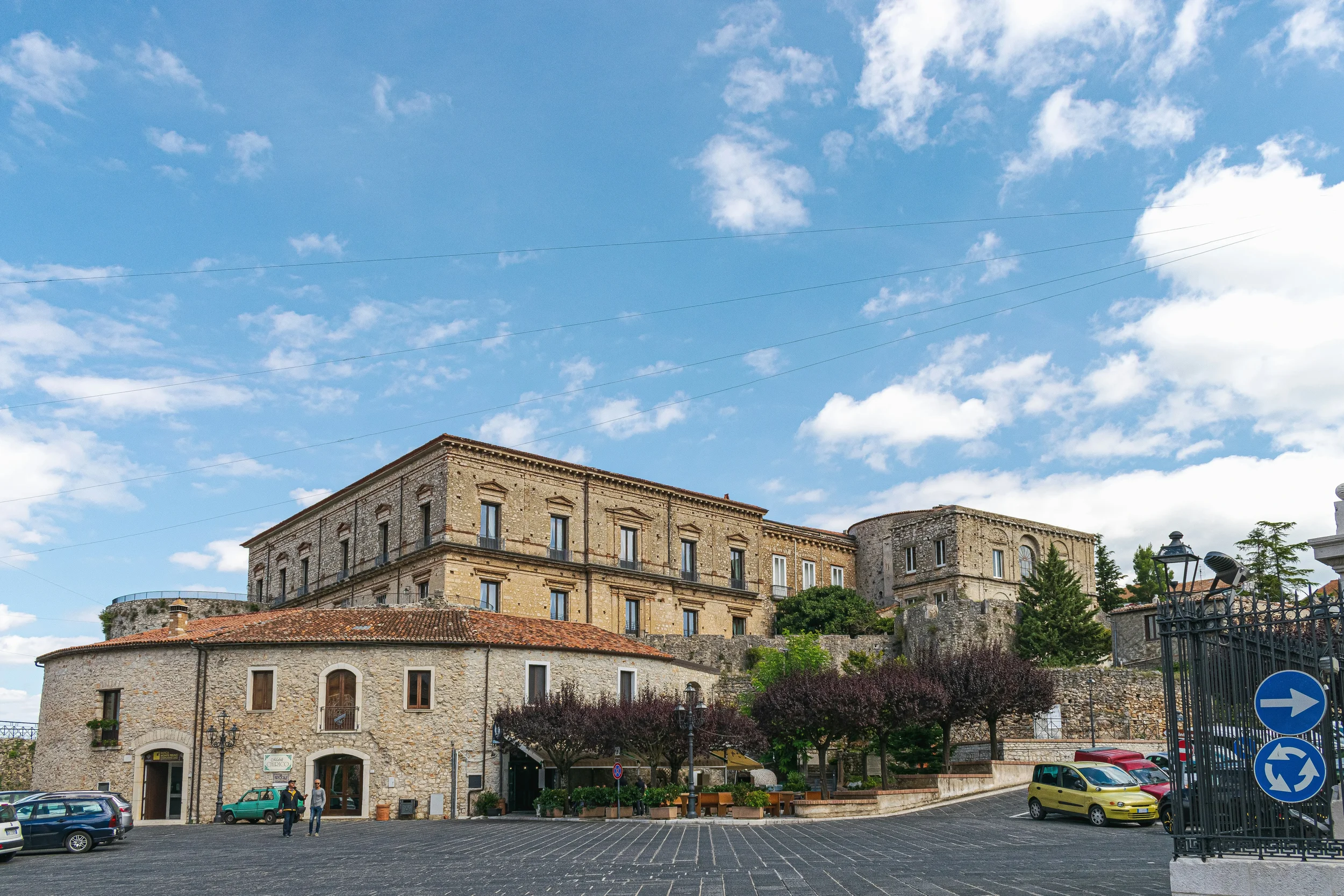 Historic stone buildings and the castle above a paved square in Teggiano.