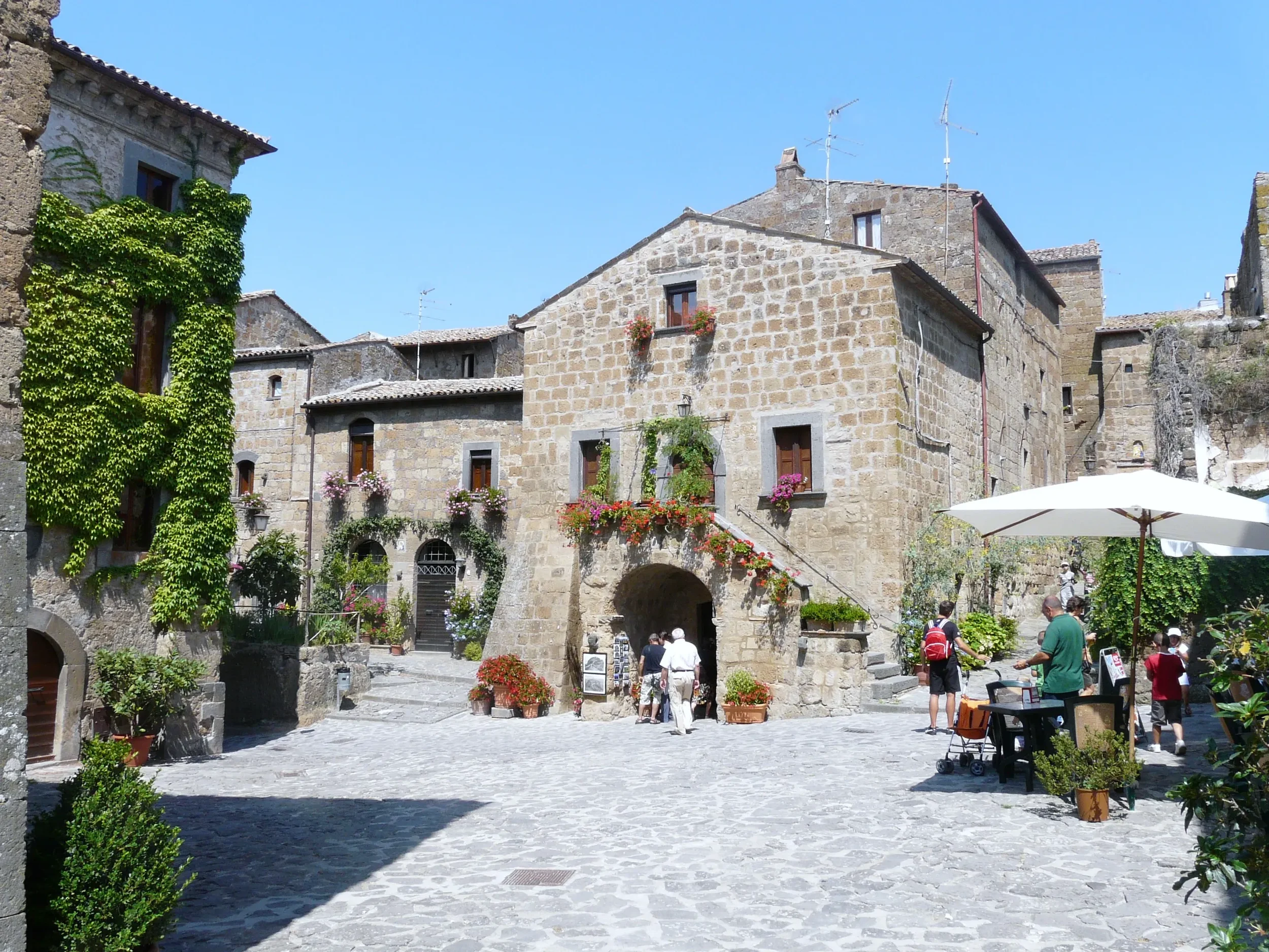 Stone houses with flower-filled balconies and ivy around a small square in Civita di Bagnoregio.