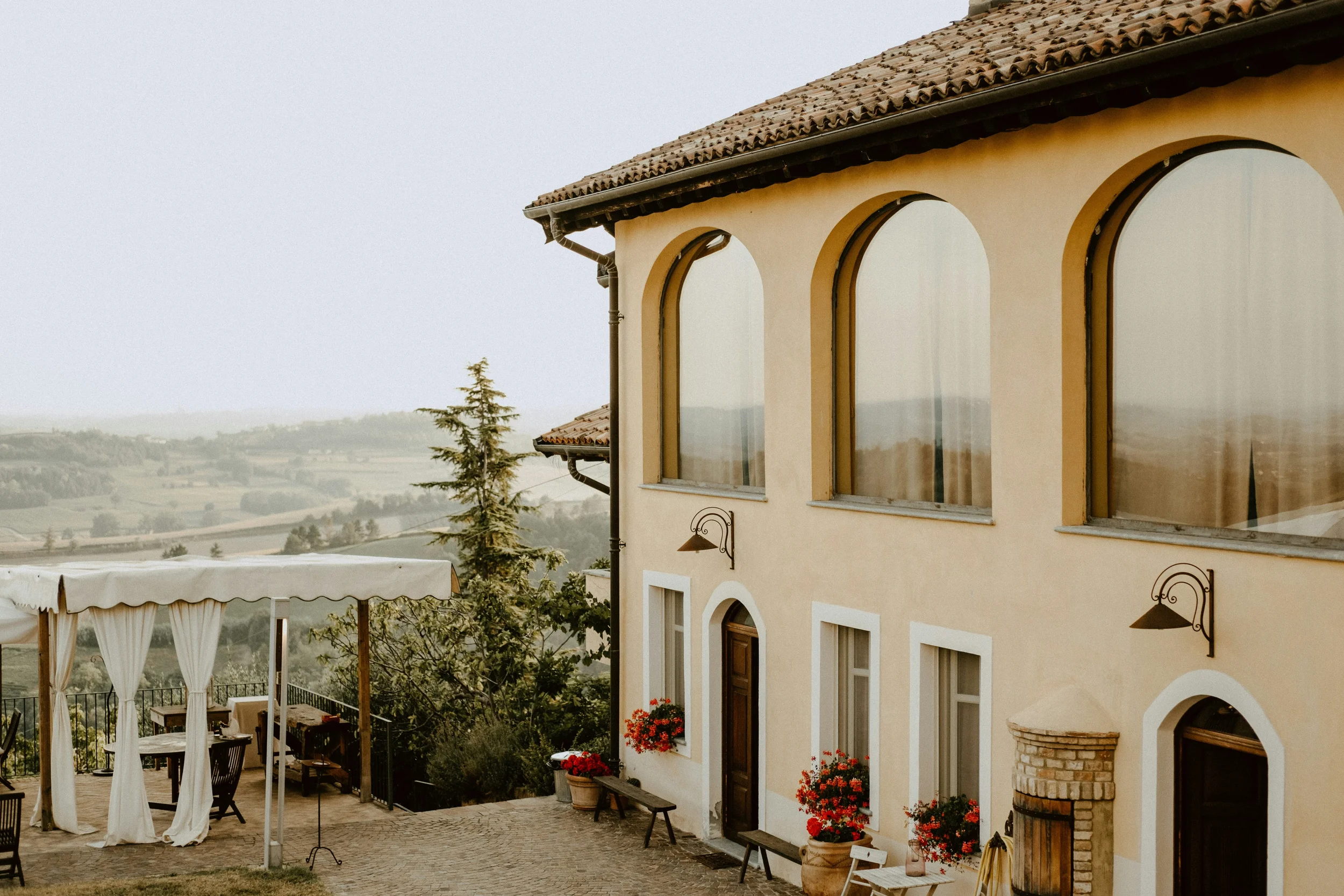 Country house with arched windows, a shaded terrace and views over rolling countryside.