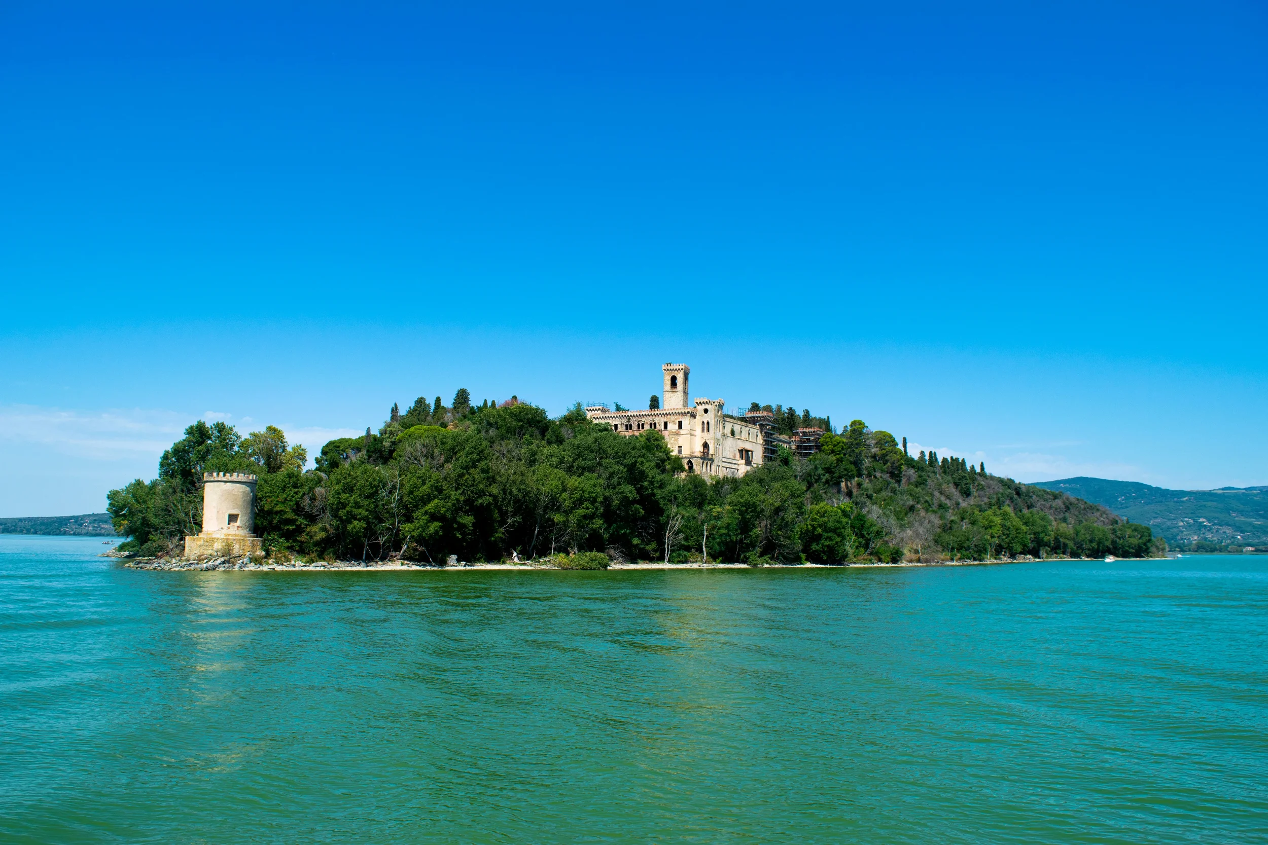 Castello Guglielmi on Isola Maggiore, surrounded by trees and the blue waters of Lake Trasimeno in Umbria.