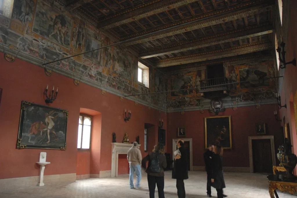 Visitors in a frescoed hall with a decorated wooden ceiling inside Castello Boncompagni Viscogliosi.