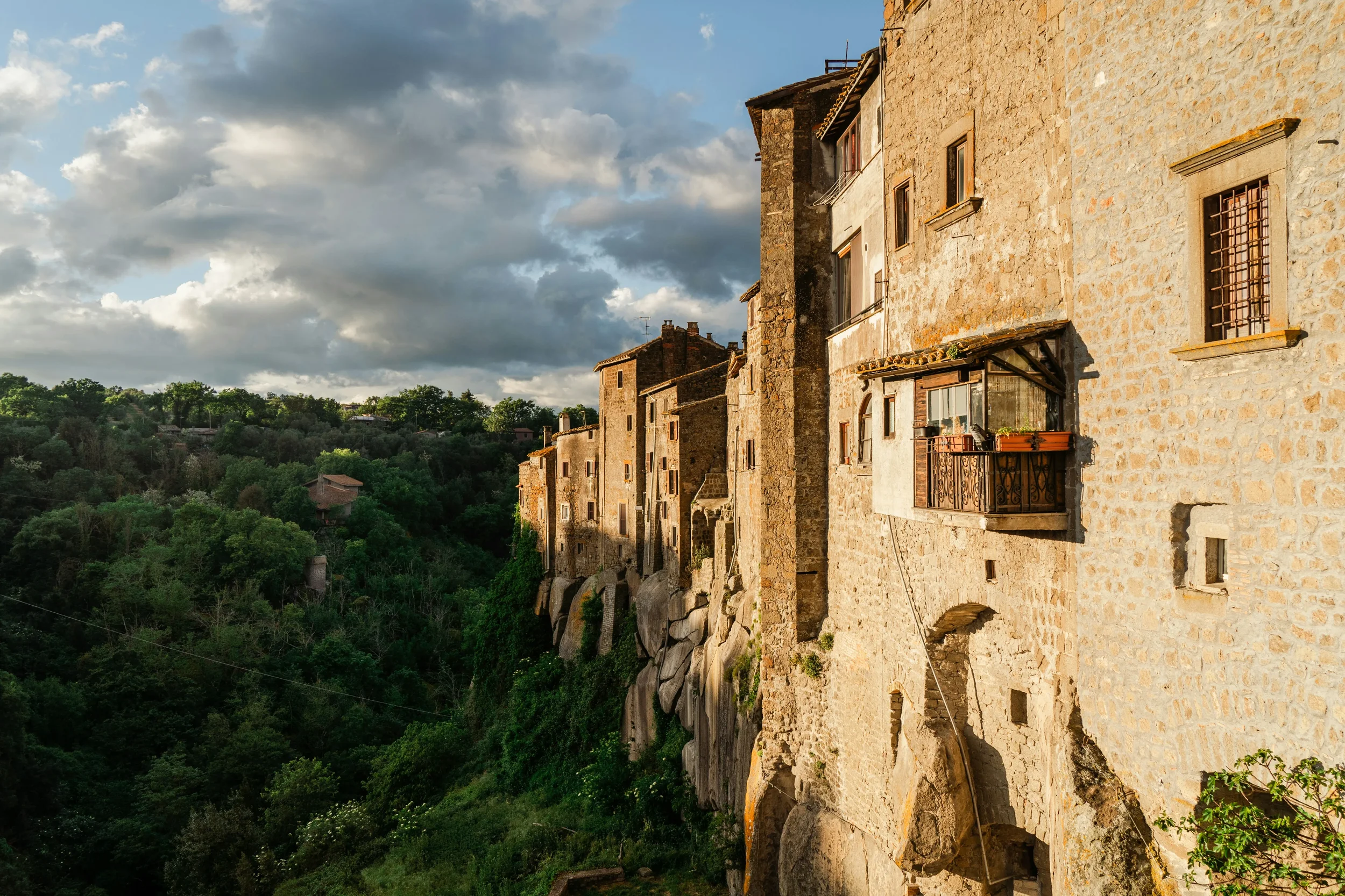 Sunlit stone houses built into the cliff above a wooded ravine in Vitorchiano.