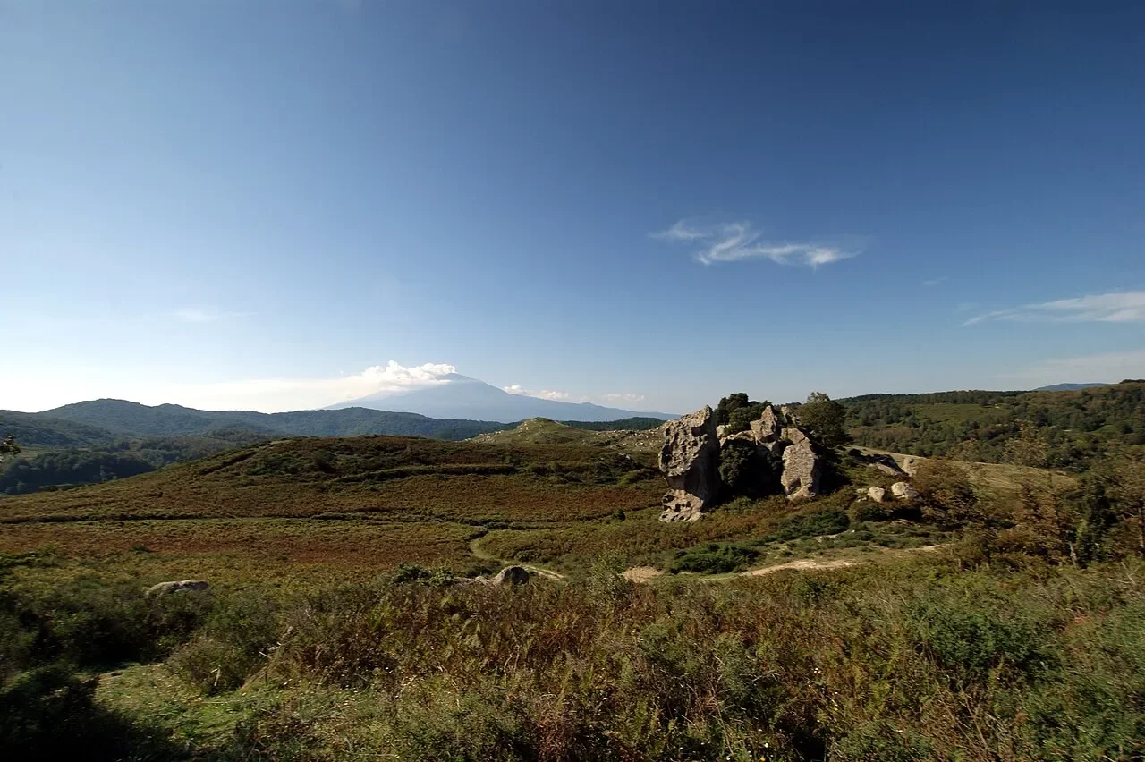 Sandstone formations on the open Argimusco plateau, with Mount Etna visible beyond the hills