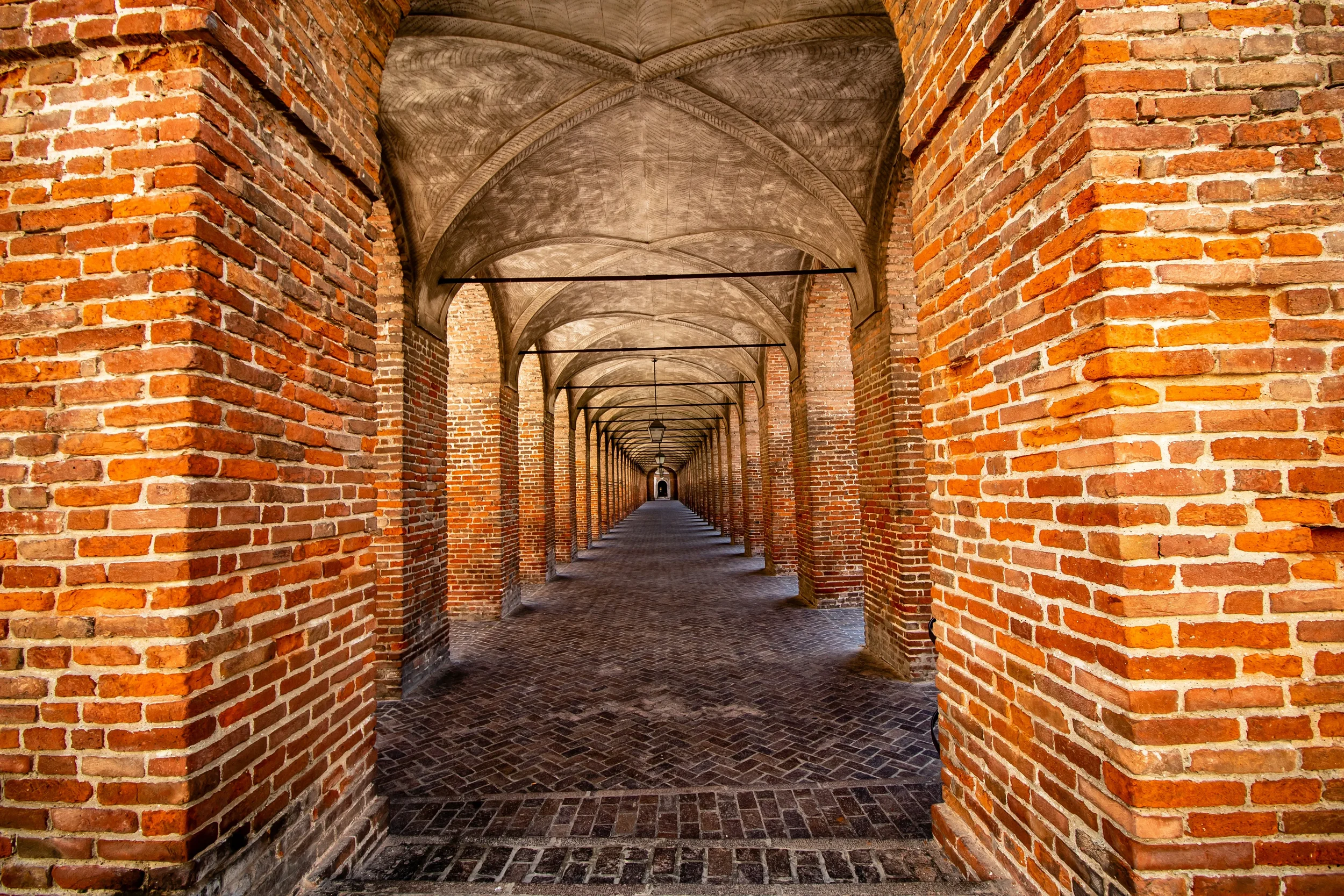 Long brick arcade with vaulted ceilings and a cobbled walkway.