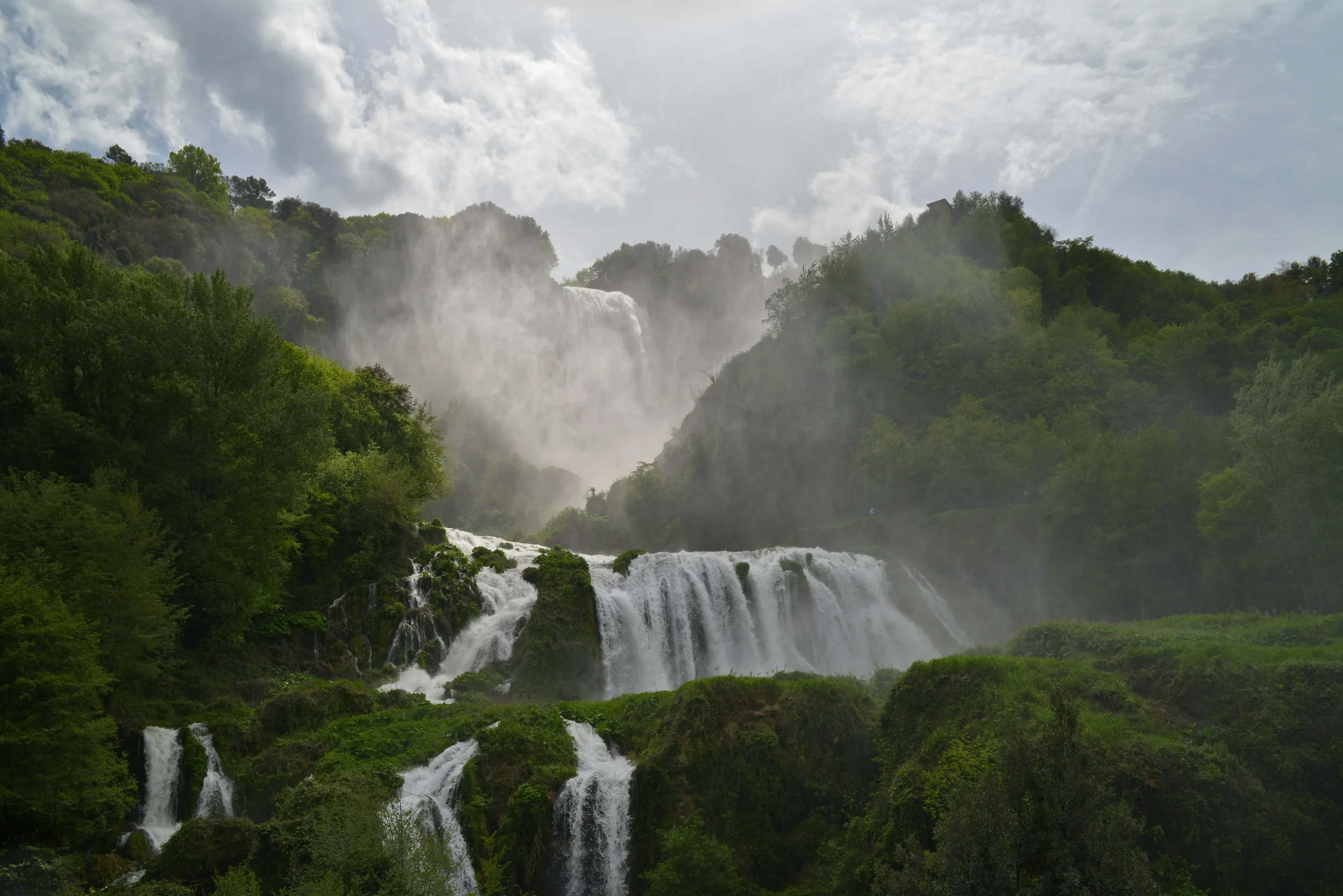 Marmore Falls cascading through green woodland, with spray rising above the lower tiers