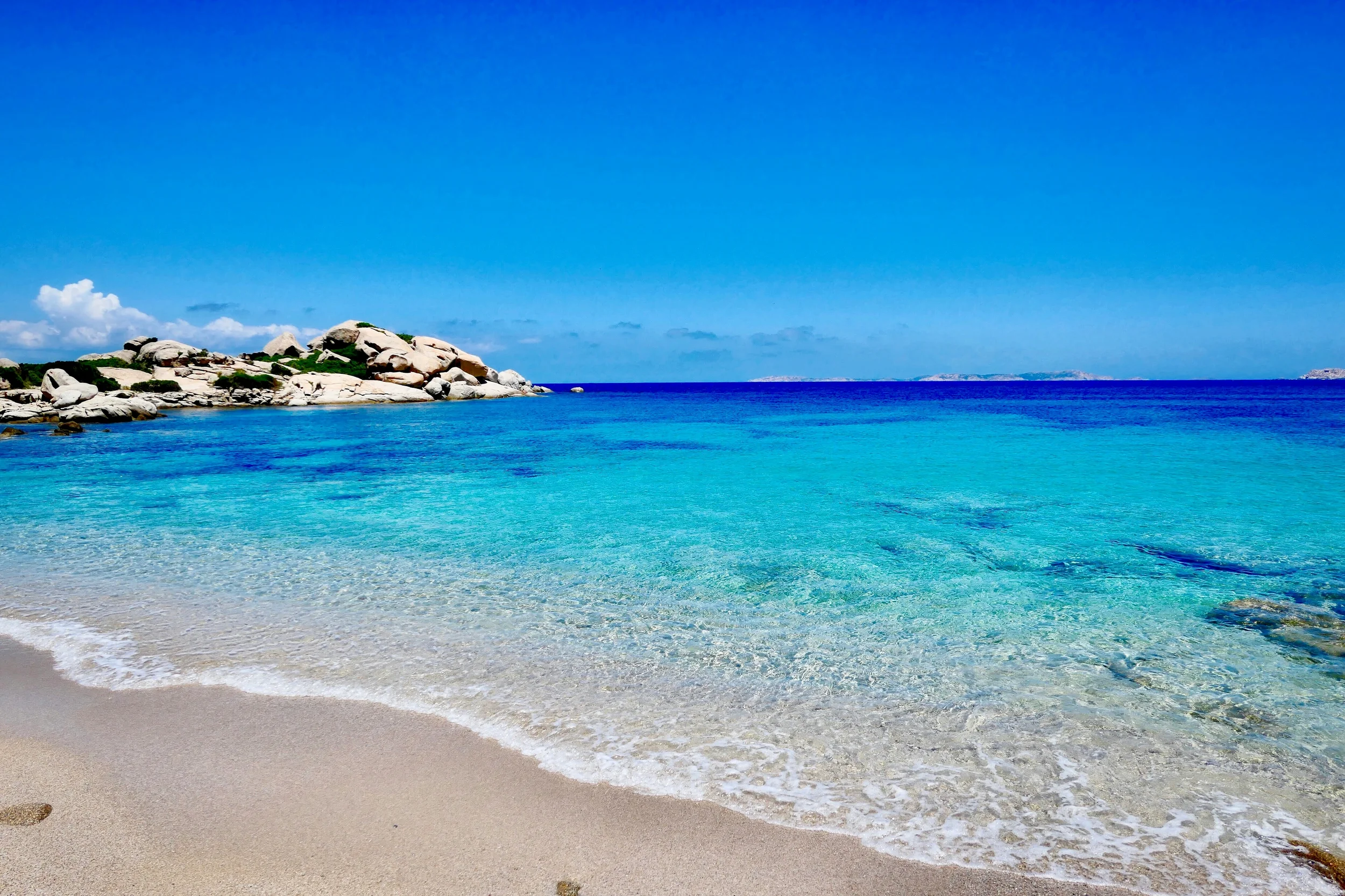 White sandy beach in Sardinia with crystal-clear turquoise water and smooth granite rocks along the coast