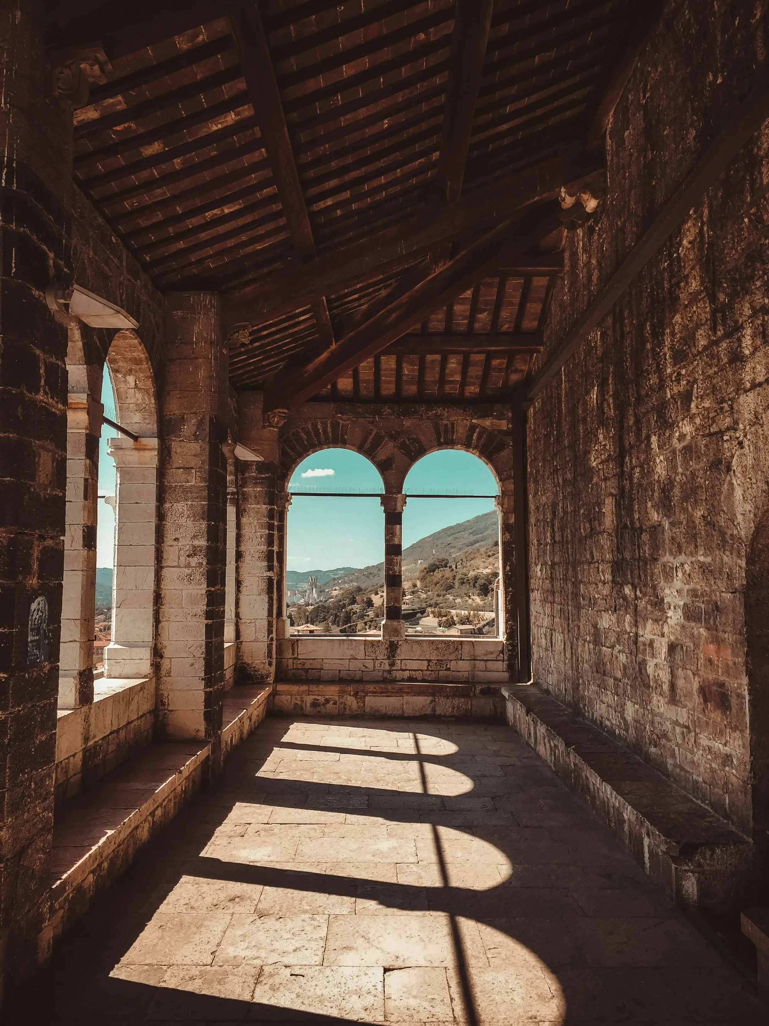 Sunlight through arched windows in a stone loggia overlooking the hills around Gubbio