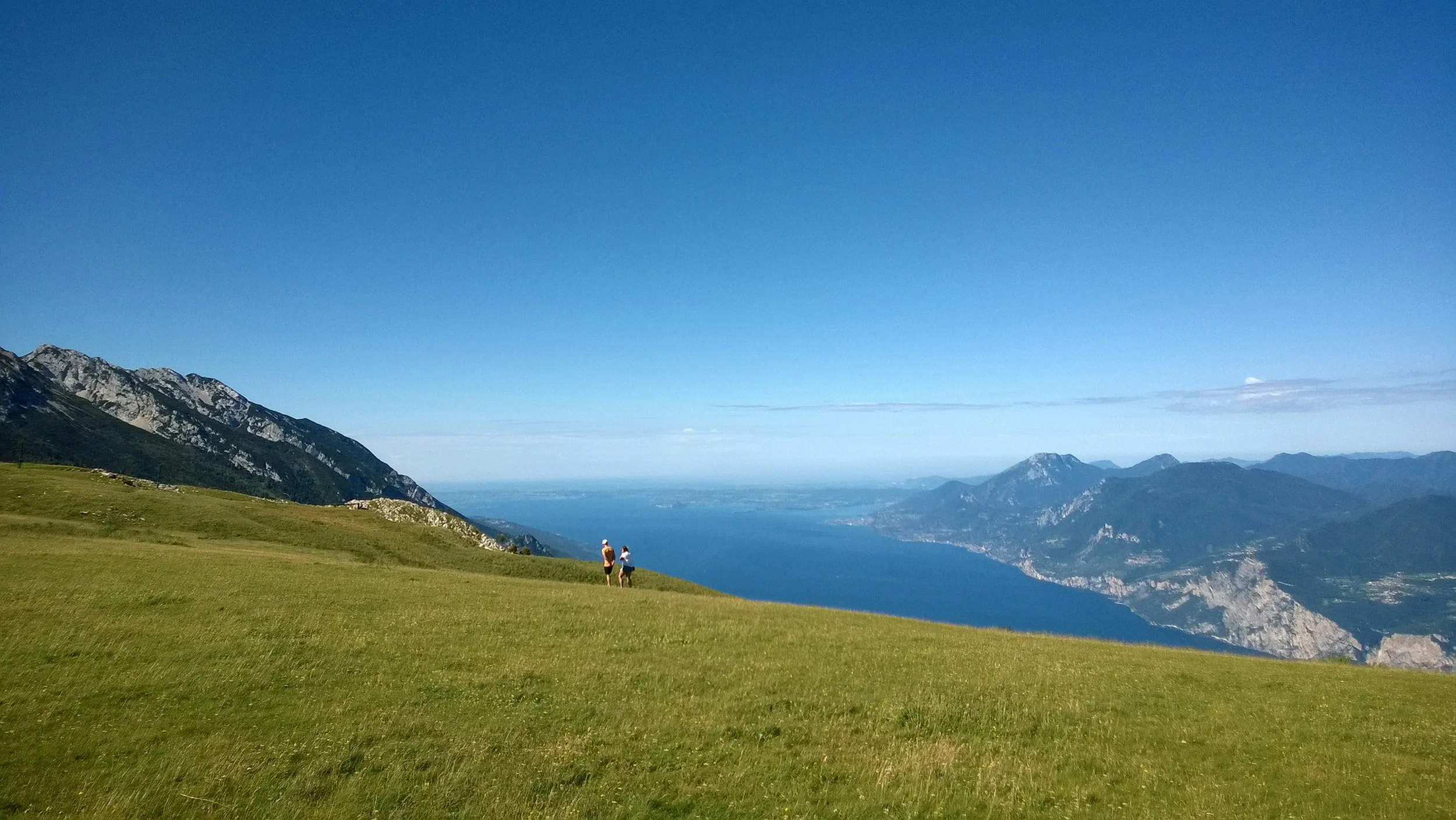 Panoramic view of Lake Garda and its mountainous shoreline from a grassy hillside