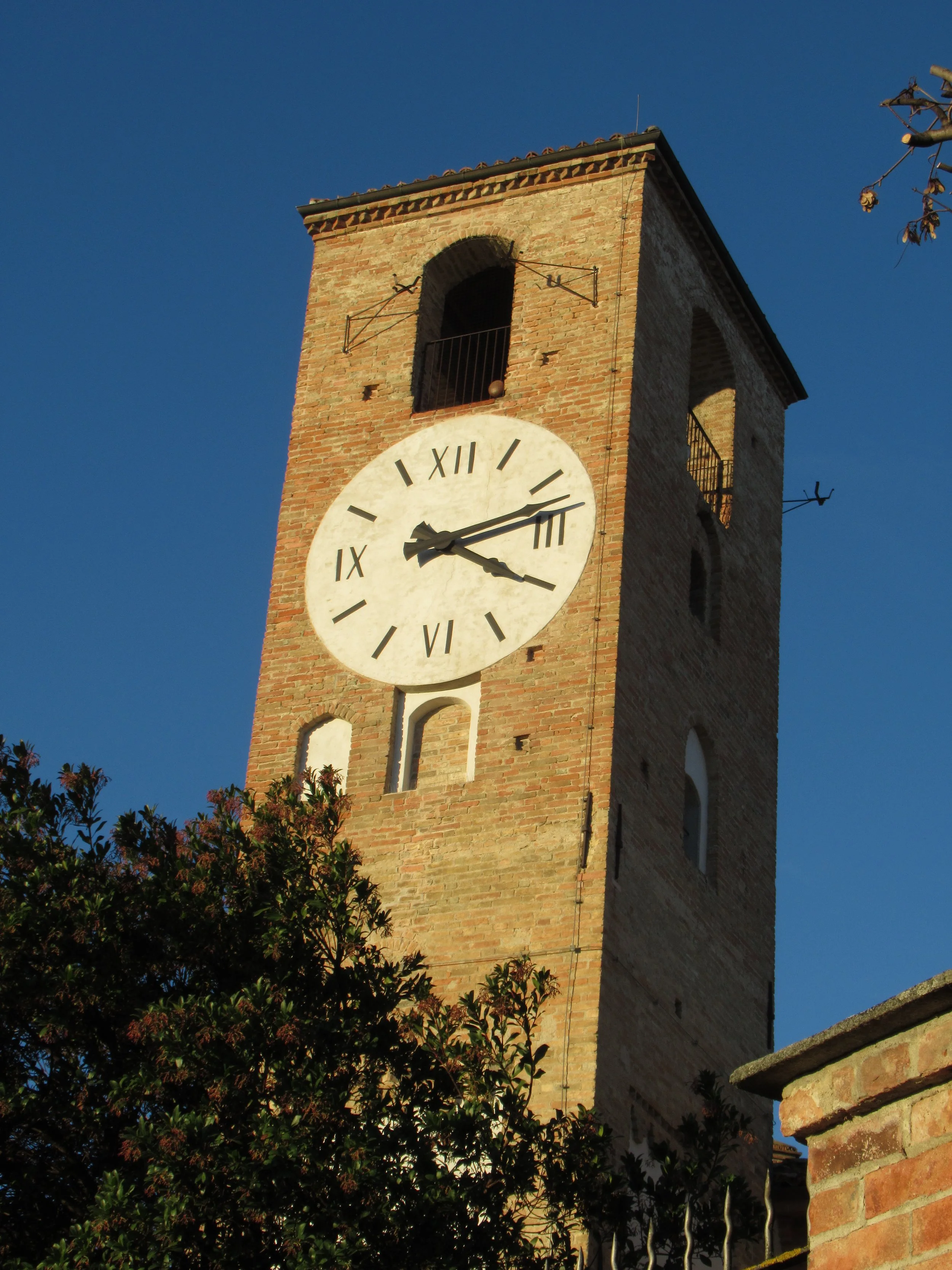 Neive’s brick Clock Tower, with a large white clock face and arched openings against a blue sky.