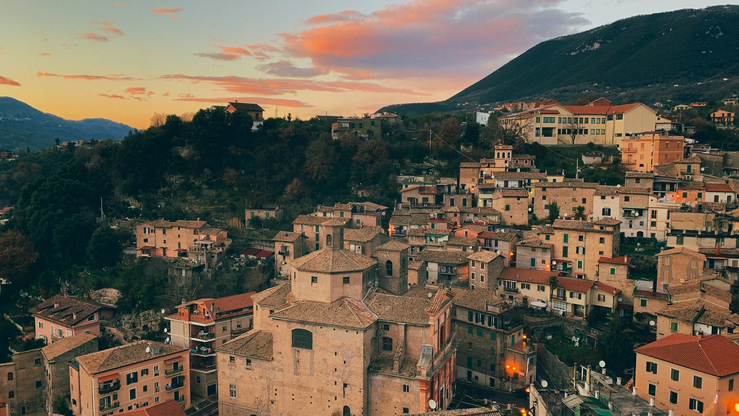 Terracotta rooftops and hillside houses in Subiaco beneath a pink and orange sunset sky.