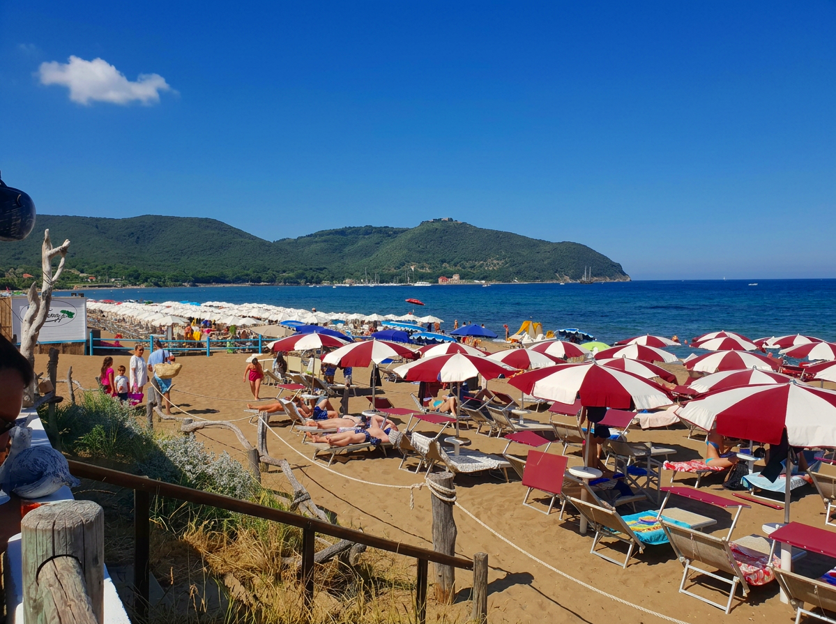 Sandy beach with colourful umbrellas and clear blue water in the Gulf of Baratti, Tuscany