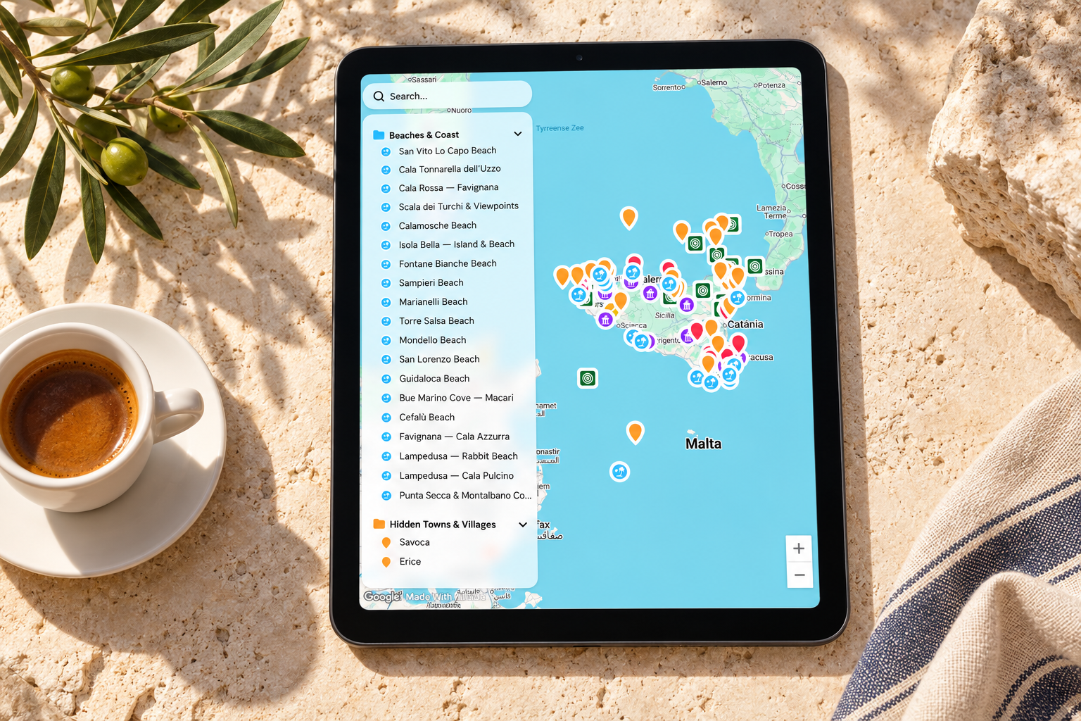 Illustrative mockup of the Hidden Italy Sicily travel map on a tablet beside an espresso and olive branches on a warm stone surface.