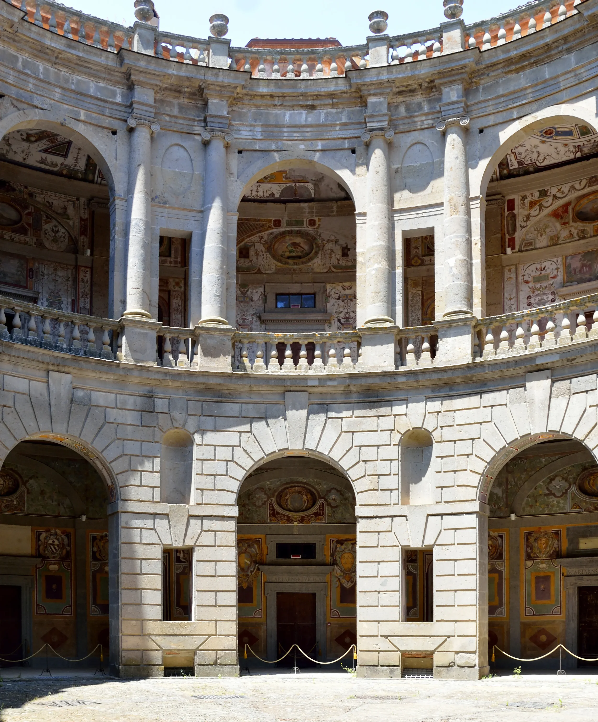 The circular courtyard of Palazzo Farnese in Caprarola, with frescoed arcades, columns and stone balustrades.