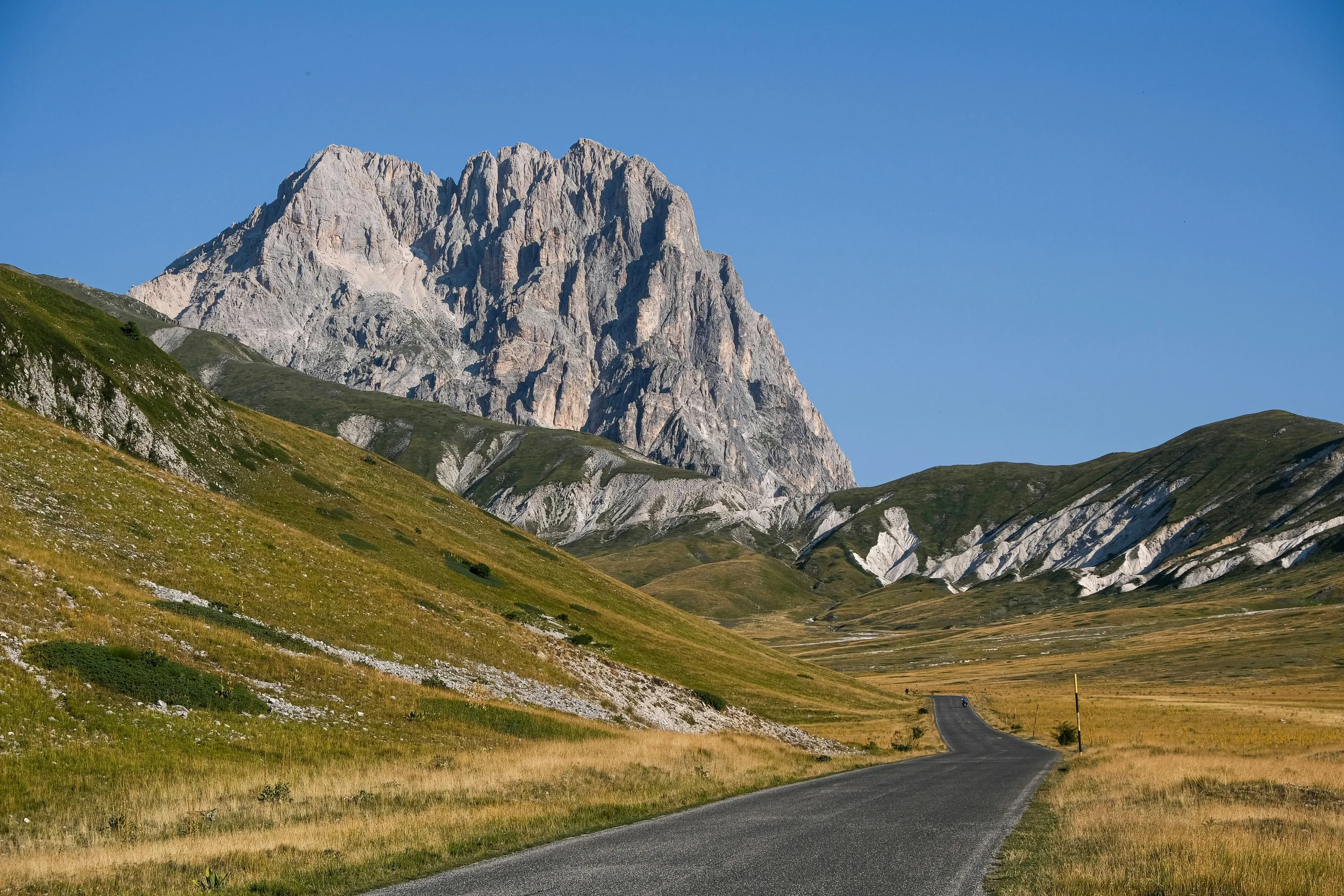 Mountain road crossing Campo Imperatore beneath the rugged peaks of Gran Sasso, Abruzzo.