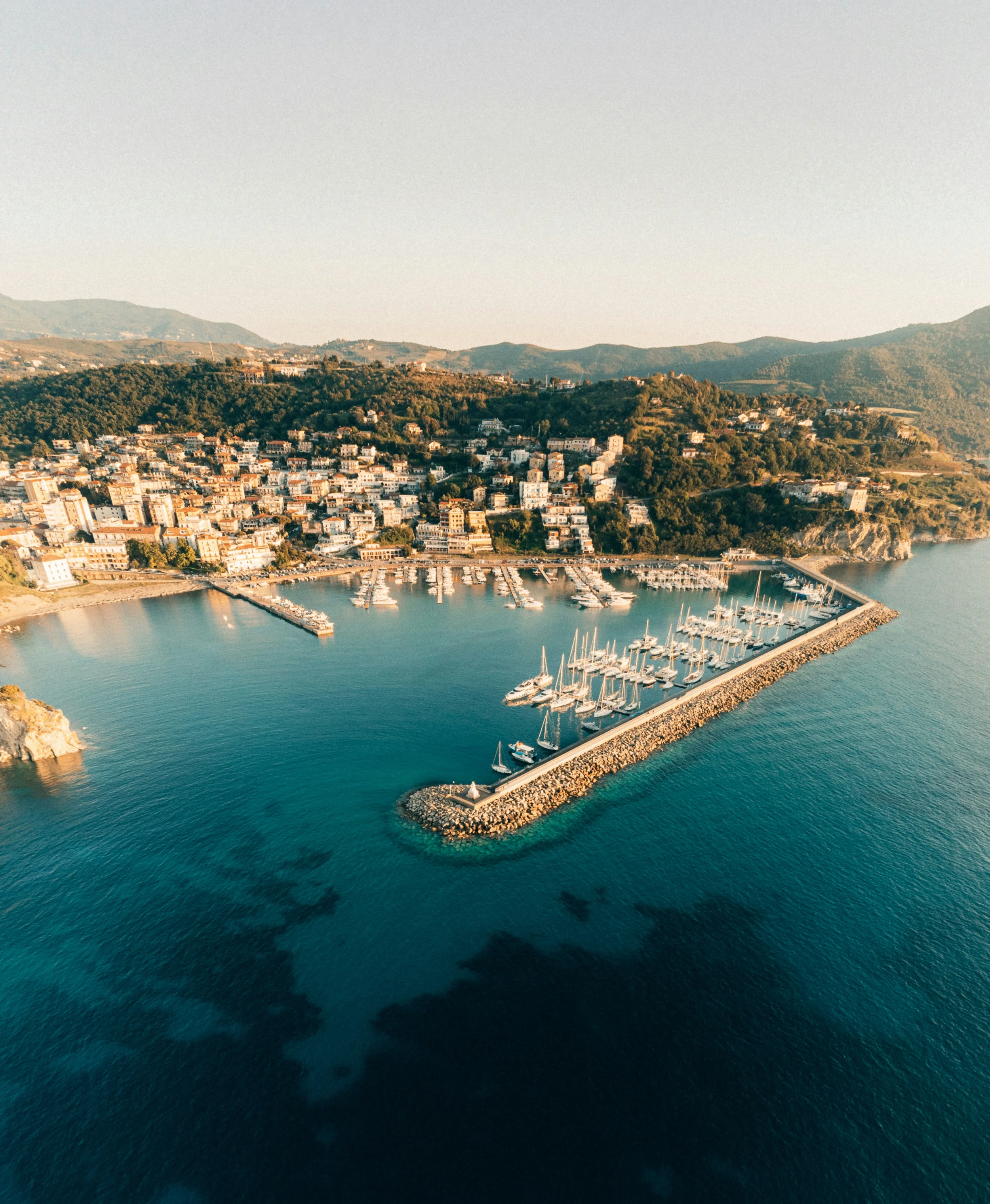 Aerial view of Agropoli harbour, its breakwater and moored boats below the coastal town.