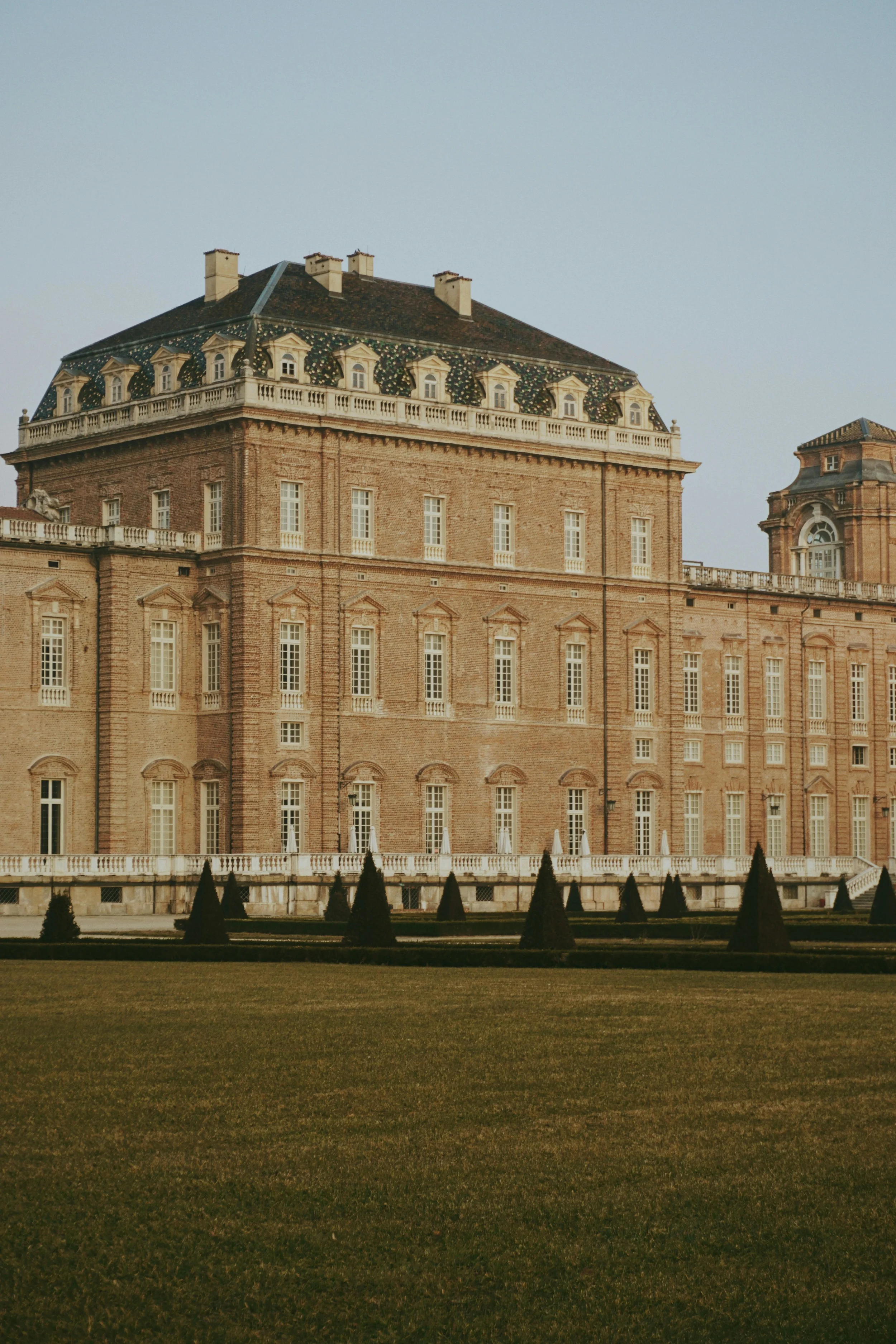 Historic brick palace facade with tall windows and formal gardens in Piemonte, Italy.