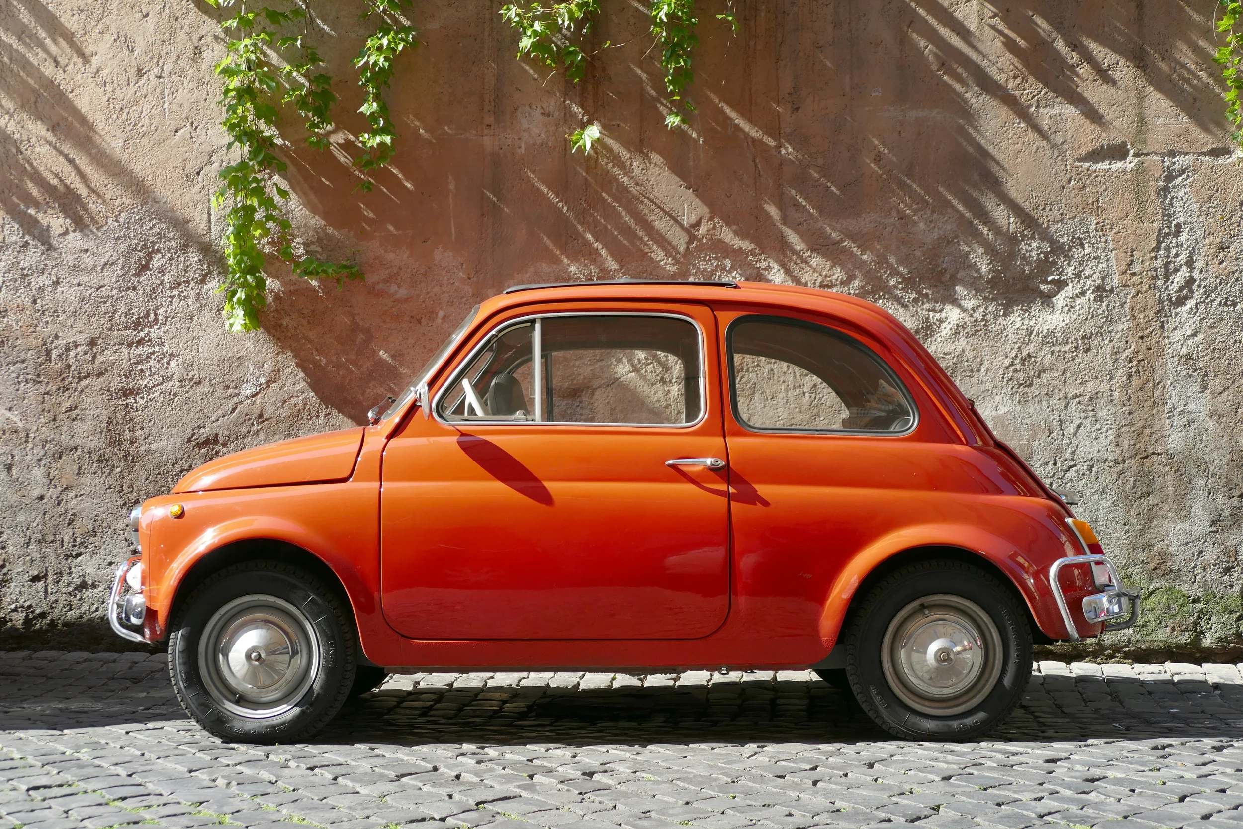 Classic red Fiat 500 parked on a cobblestone street in Italy
