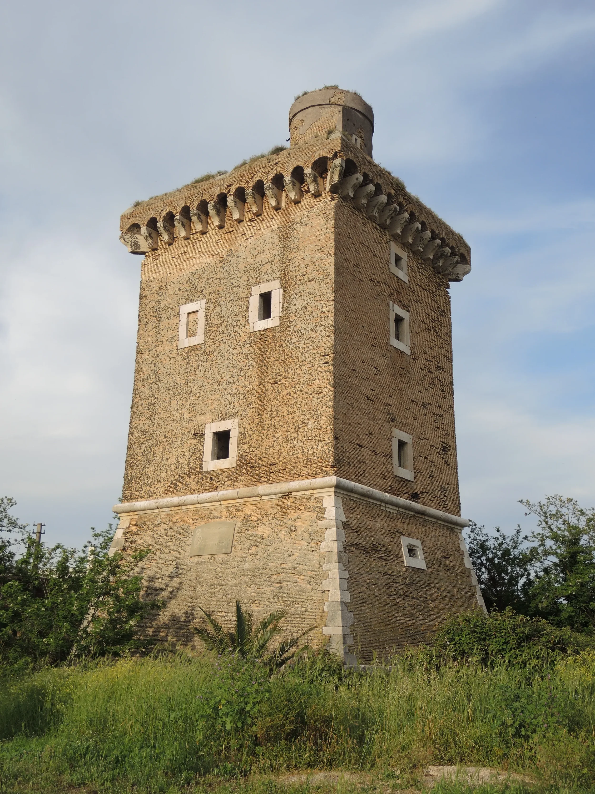 The square stone Torre Olevola rising above grass and shrubs near San Felice Circeo.