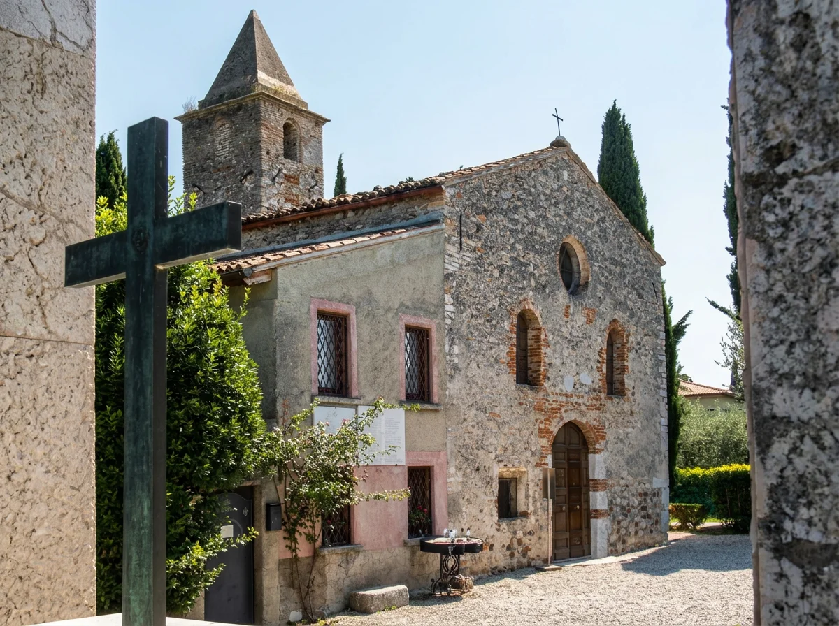 Stone church façade and bell tower framed by trees, with a large dark cross in the foreground.