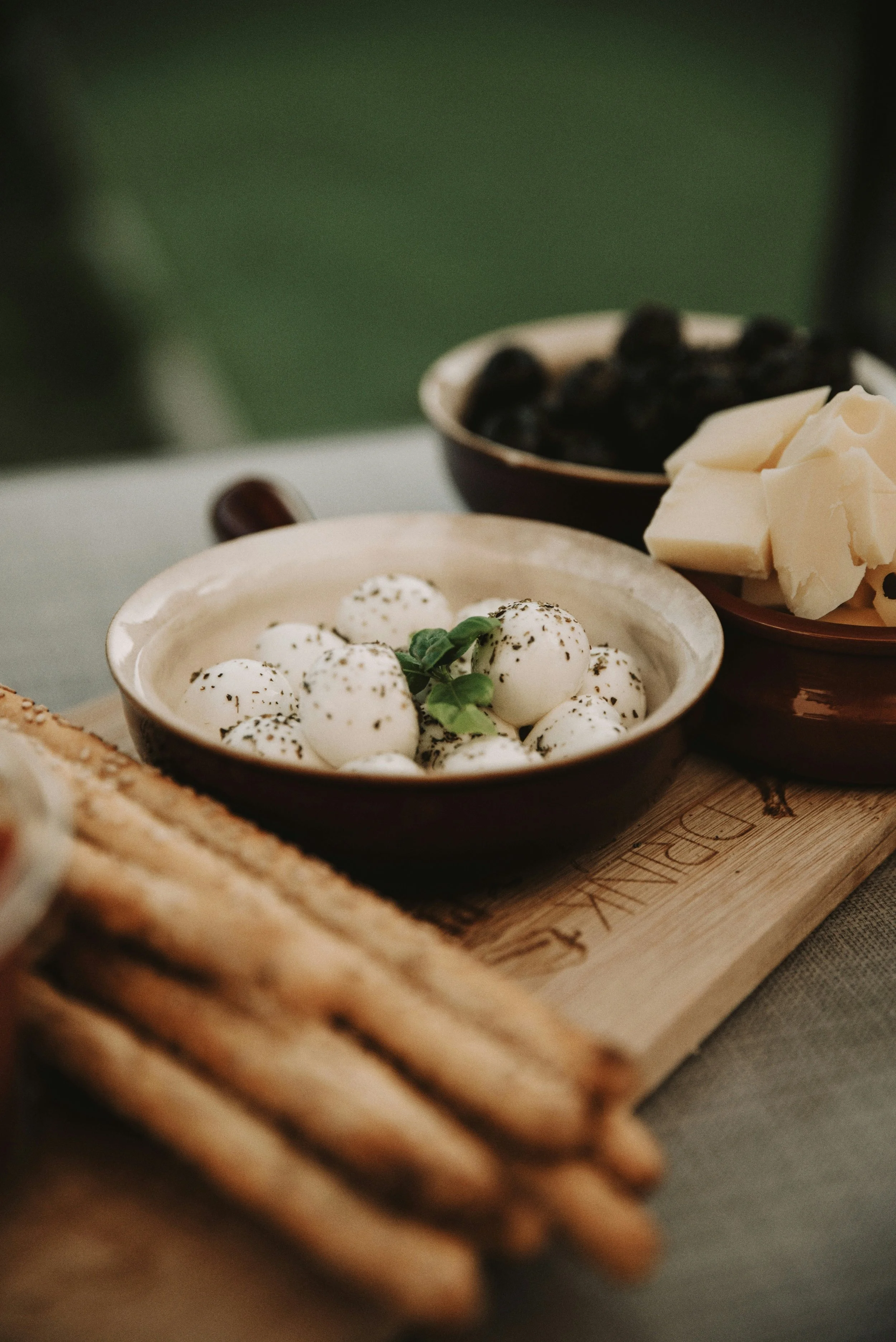 Mozzarella with herbs in a bowl, served with toasted bread, olives and cheese on a wooden board.